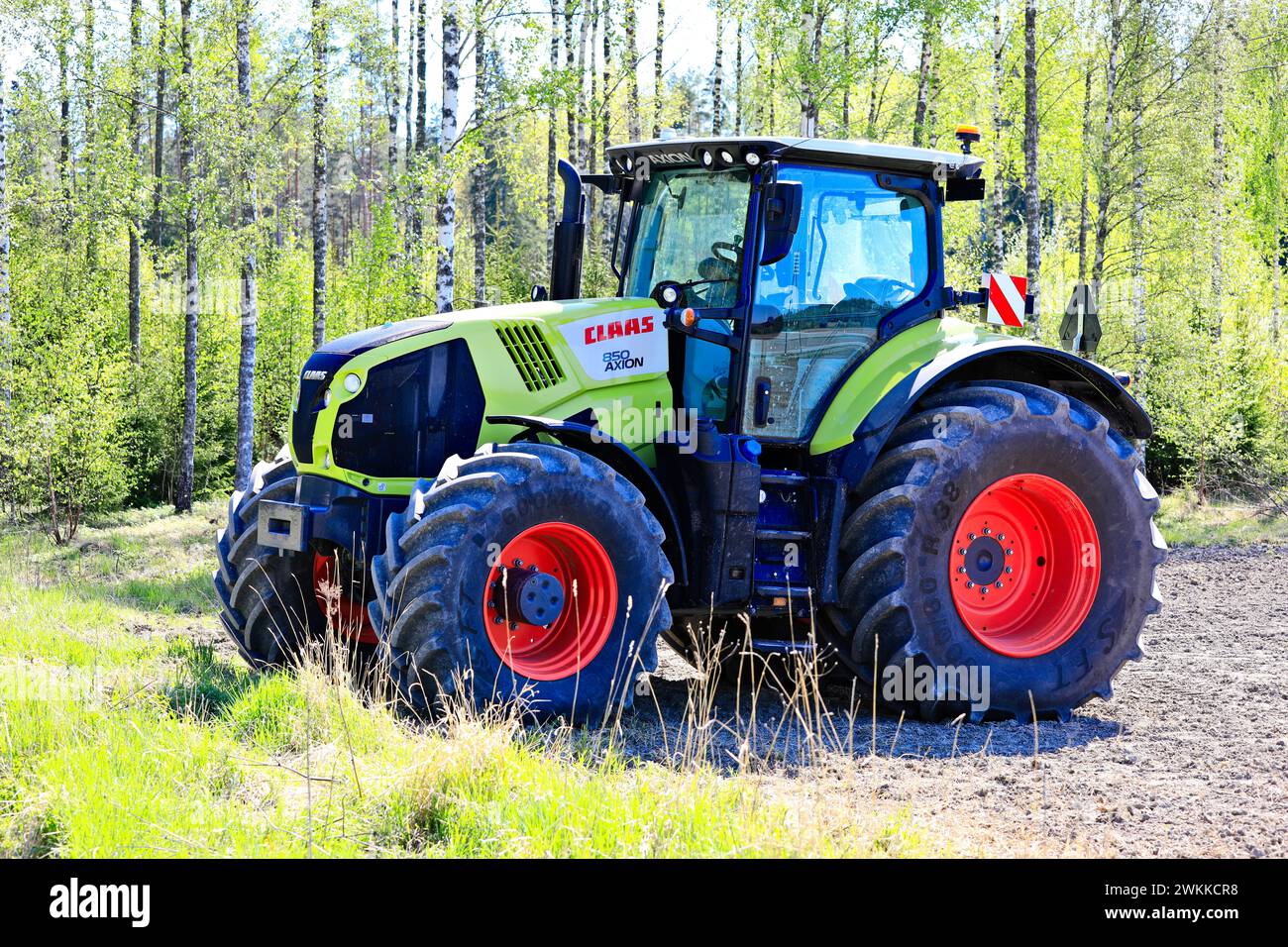 Claas Axion 850 Traktor auf dem Feld an einem sonnigen Frühlingstag, grüner Birkenwald Hintergrund. Salo, Finnland. Mai 2023. Stockfoto