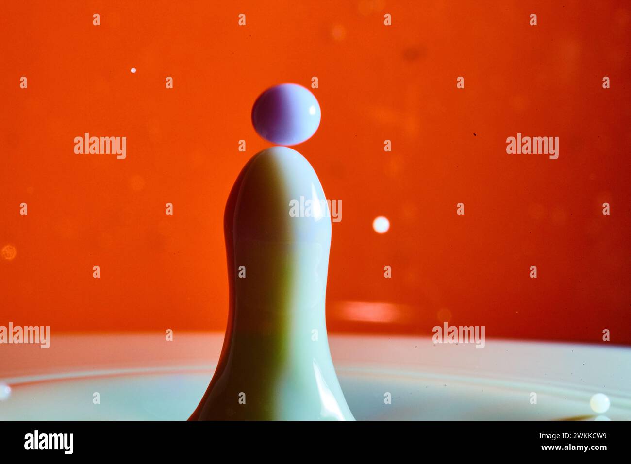Eleganter Milk Drop Collision auf leuchtendem orangefarbenem Hintergrund Stockfoto