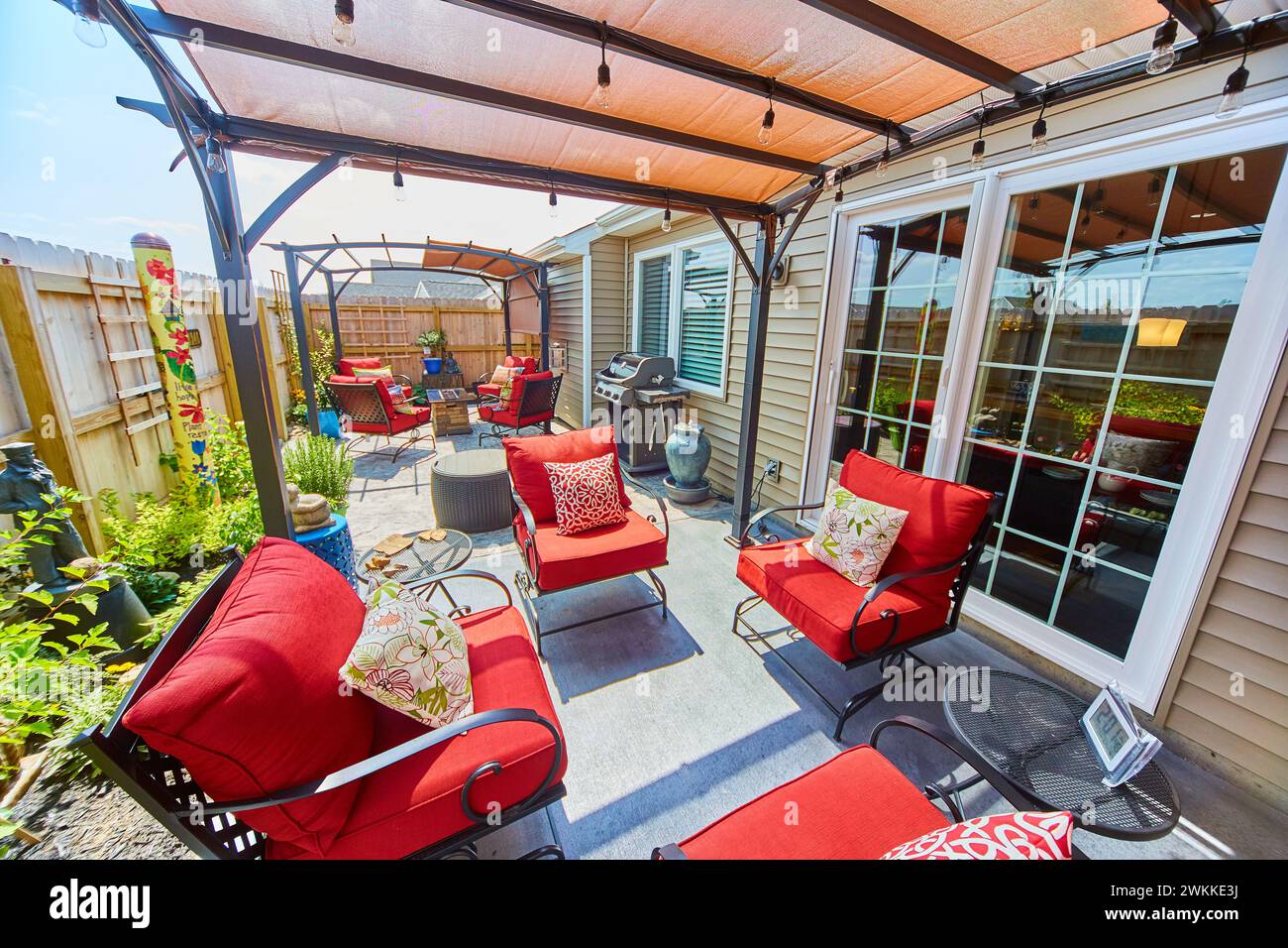 Sonnige Wohnterrasse mit roten Kissen und Pergola Stockfoto