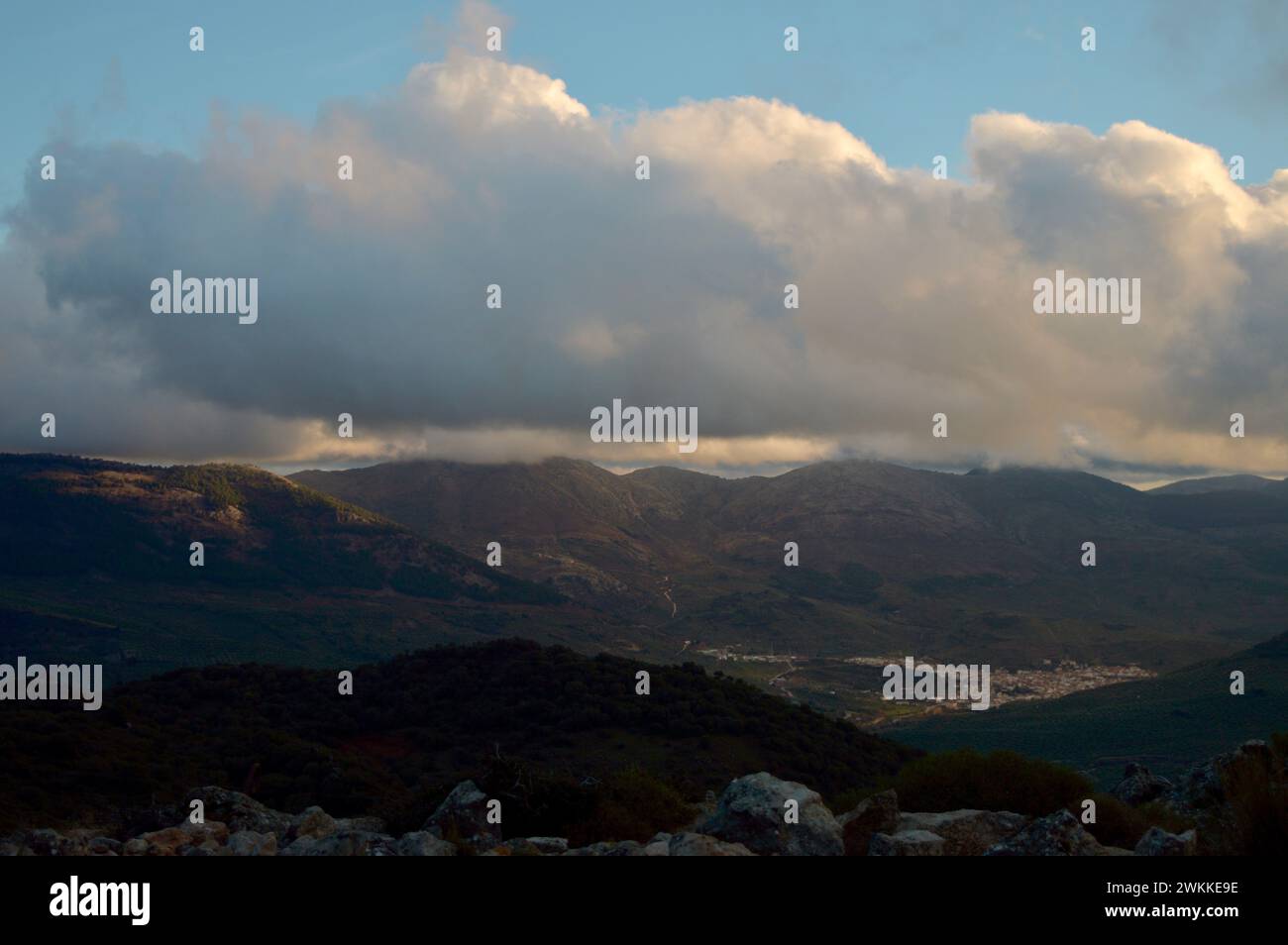 Flauschige Wolken über einer Bergstadt mit Sonnenstrahlen, die den Bergen einen himmlischen Glanz verleihen. Stockfoto