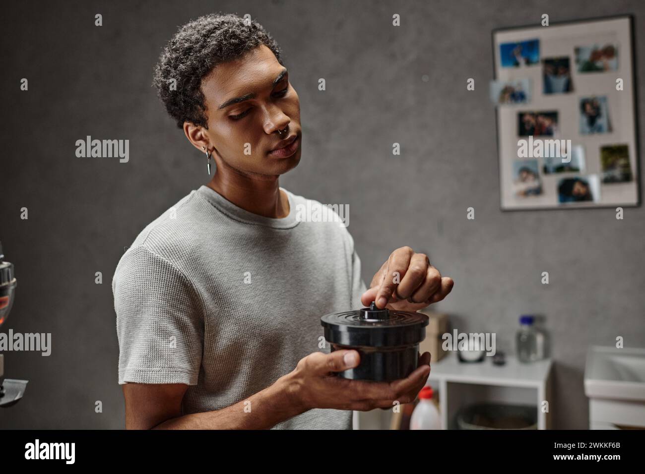 Junger afroamerikanischer Mann, der einen Filmkanisterdeckel in der Dunkelkammer sichert, traditionelle Fotografie Stockfoto