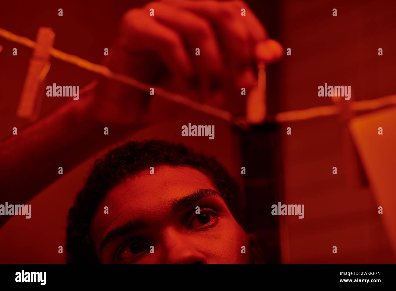 Junger afroamerikaner hängt frisch entwickelten Filmstreifen in einer rot beleuchteten Dunkelkammer, Nostalgie Stockfoto