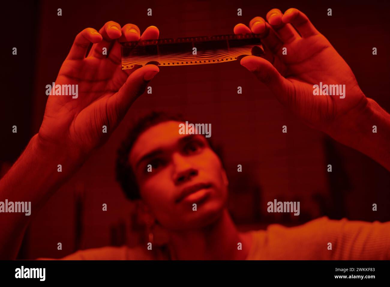Fokussierter afroamerikanischer Fotograf untersucht den entwickelten Filmstreifen in einer rot beleuchteten Dunkelkammer Stockfoto