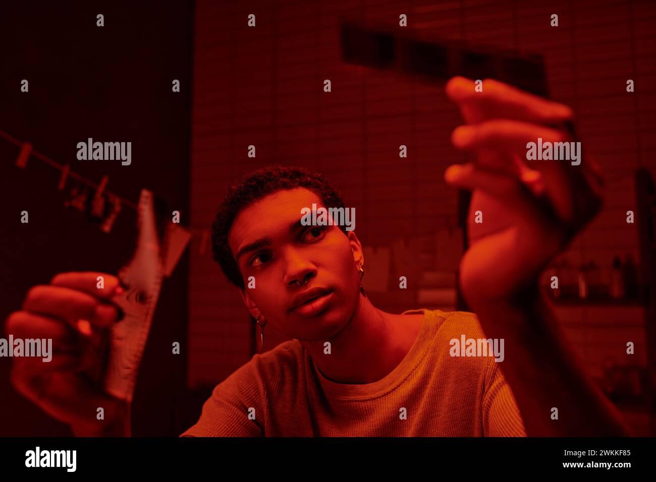Konzentrierter afroamerikanischer Fotograf, der entwickelte Filmstreifen in einer rotbeleuchteten Dunkelkammer vergleicht Stockfoto