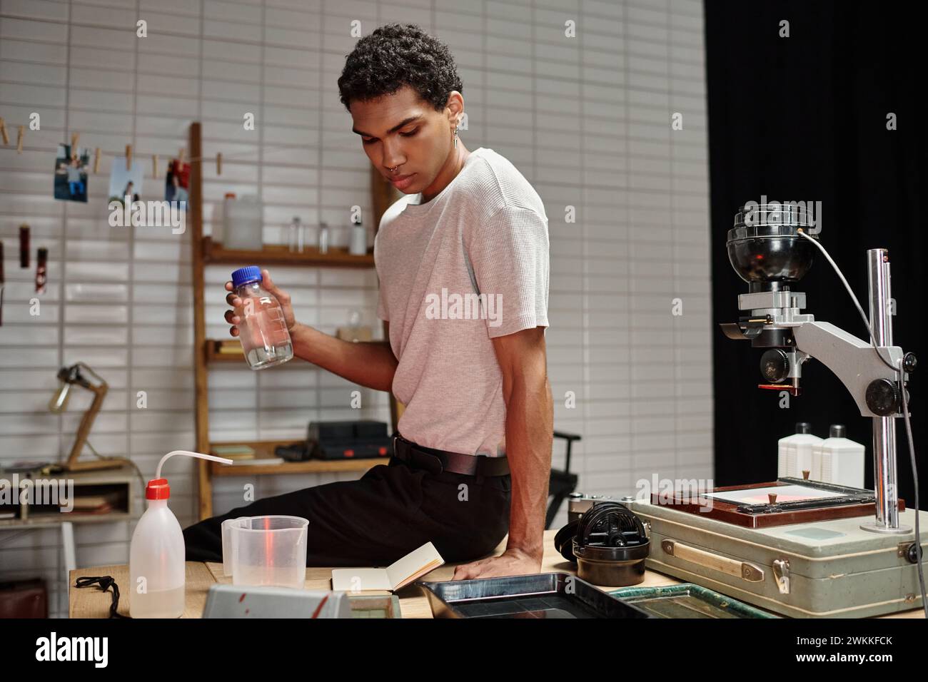 Schöner afroamerikanischer Fotograf, der Flasche mit chemischer Lösung hält, Filmentwicklung Stockfoto