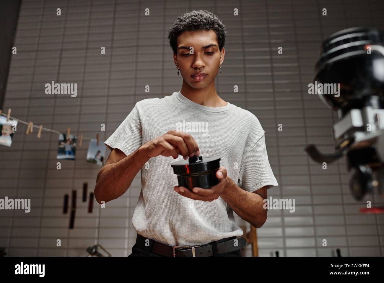 Junger afroamerikanischer Fotograf, der Filmkanisterdeckel in der Dunkelkammer sichert, analoge Entwicklung Stockfoto