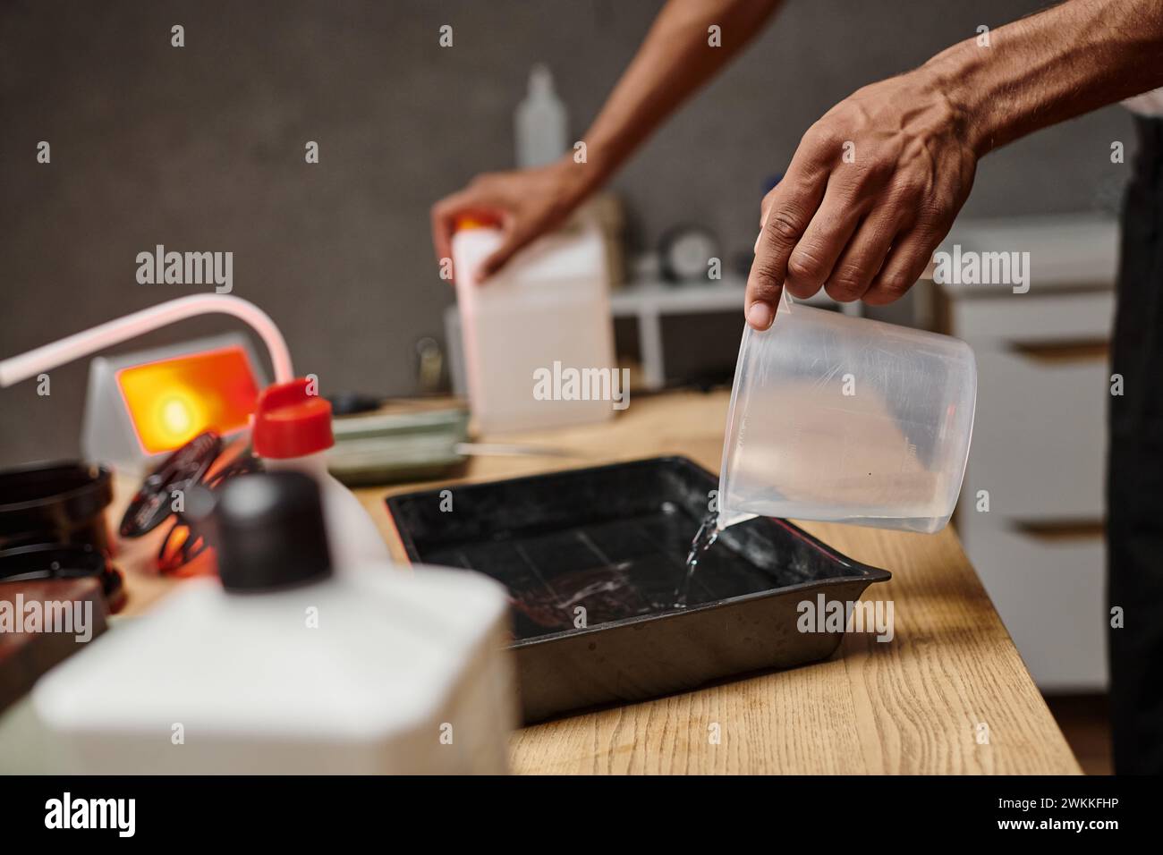Zugeschnittene Aufnahme eines afroamerikanischen Fotografen, der chemische Lösung für die Filmentwicklung eingießt Stockfoto