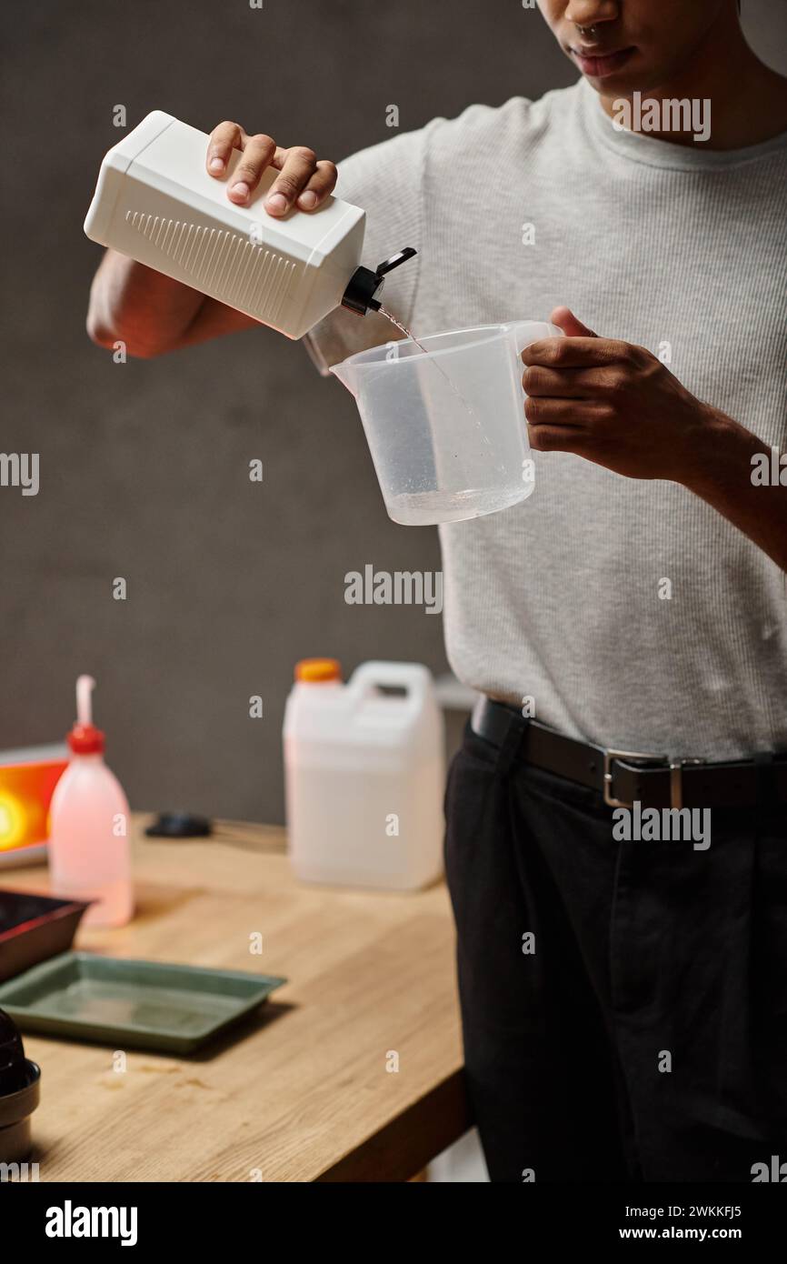 Zugeschnittener afroamerikanischer Mann, der chemische Lösung in Messbecher gießt, Filmentwicklung Stockfoto