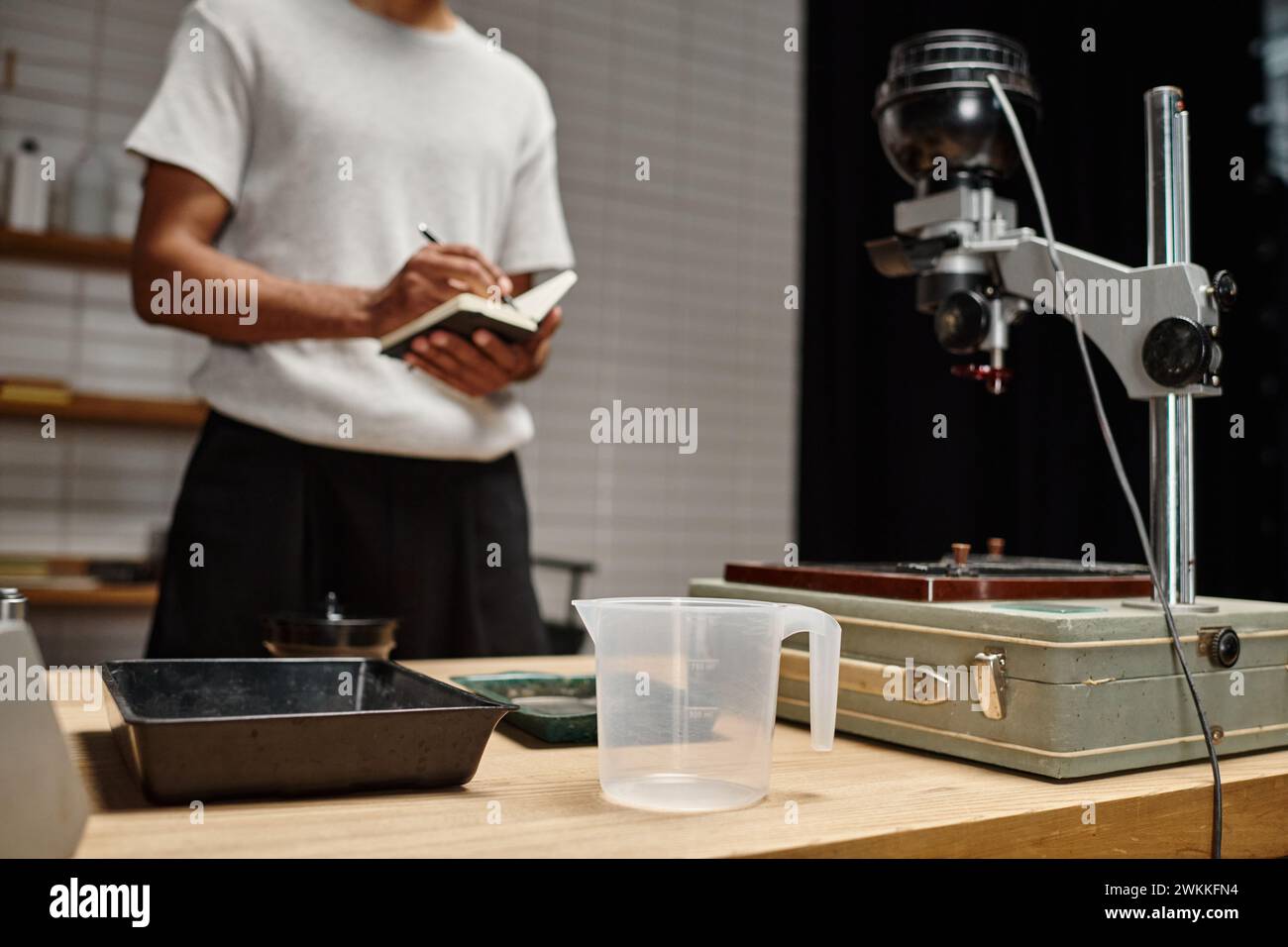 Filmtablett und andere Fotoentwicklungsgeräte in der Nähe eines Schwarzen Mannes mit Notebook in einer Dunkelkammer Stockfoto