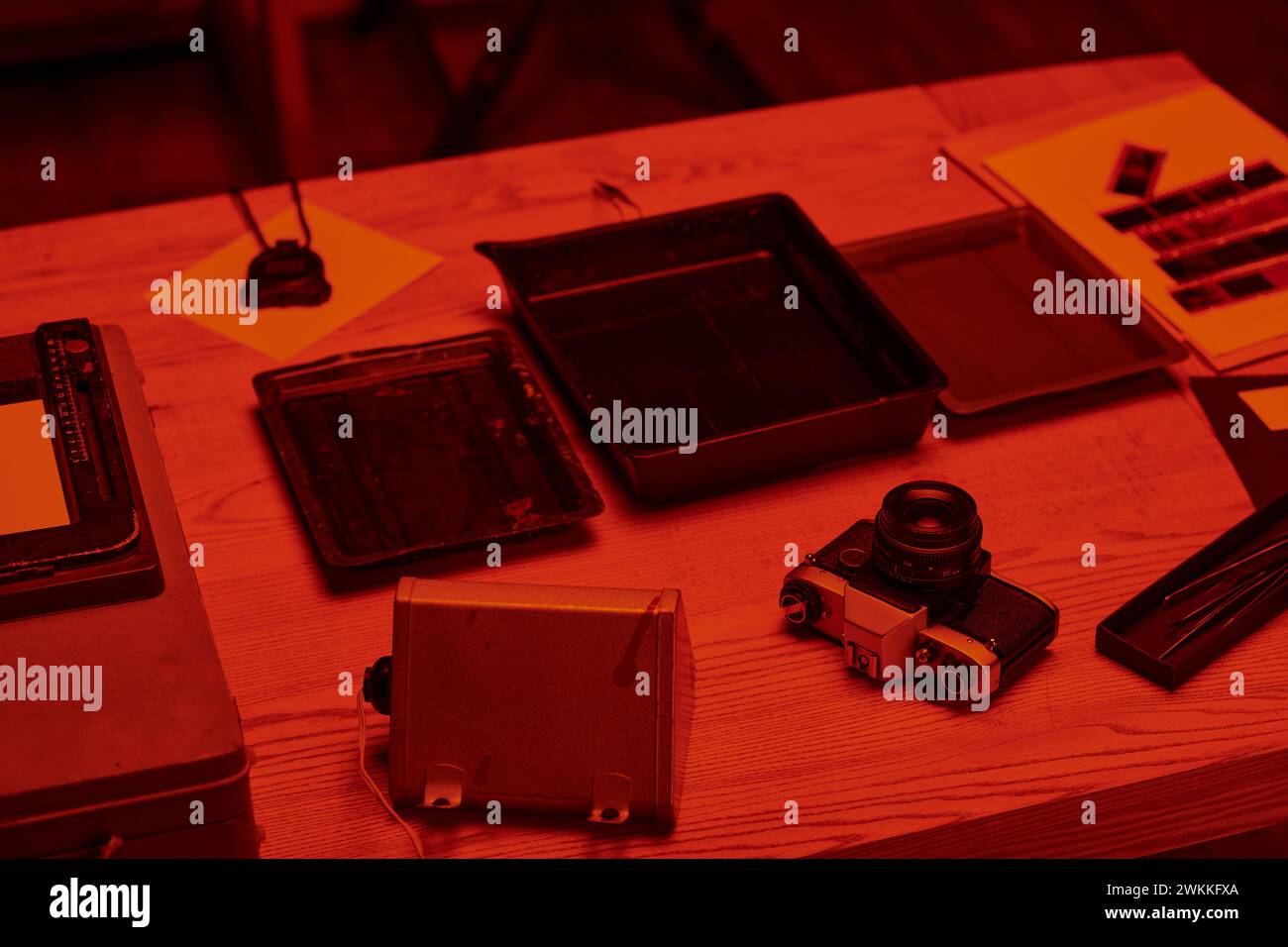 Ein Tisch mit analoger Kamera und Werkzeugen für die Filmentwicklung in Dunkelkammer mit rotem Licht, Nostalgie Stockfoto