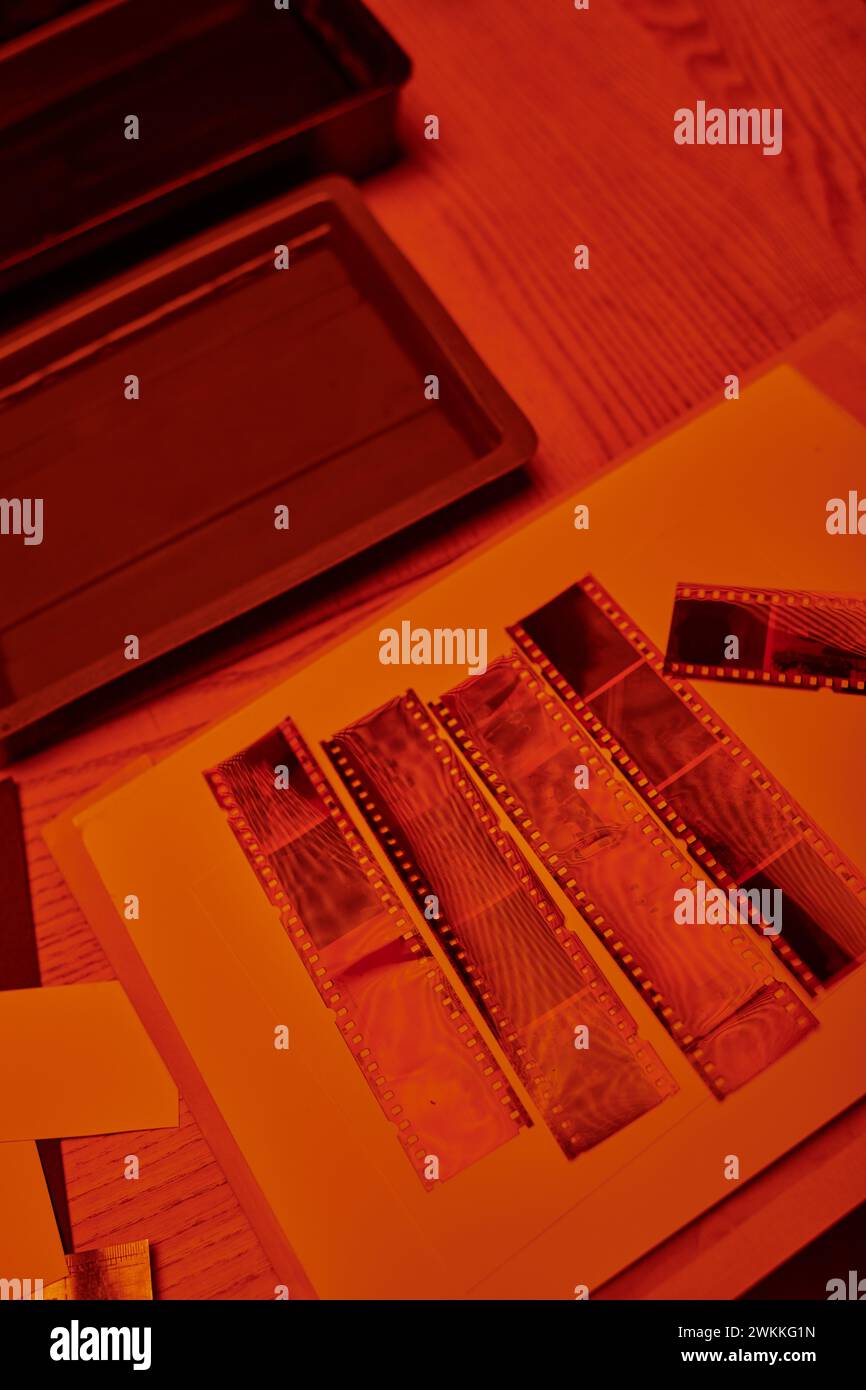 Entwickelte Filmstreifen auf einem Tisch neben Dunkelkammer-Fotoausrüstung, in rotem Sicherheitslicht Stockfoto