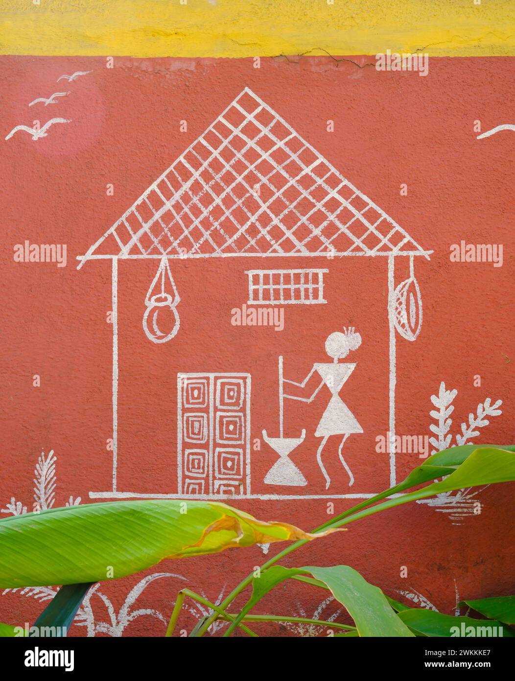 Warli-Tribal-Illustration, die eine Frau zeigt, die vor einer Hütte auf einer Gartenwand gemalt ist Stockfoto