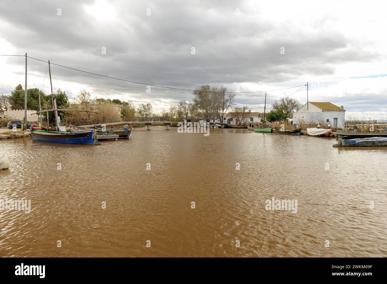 Traditionelle Boote legten an einem schlammigen Ufer unter einem dramatischen, wolkenverhangenen Himmel an und zeigen eine ruhige ländliche Landschaft Stockfoto