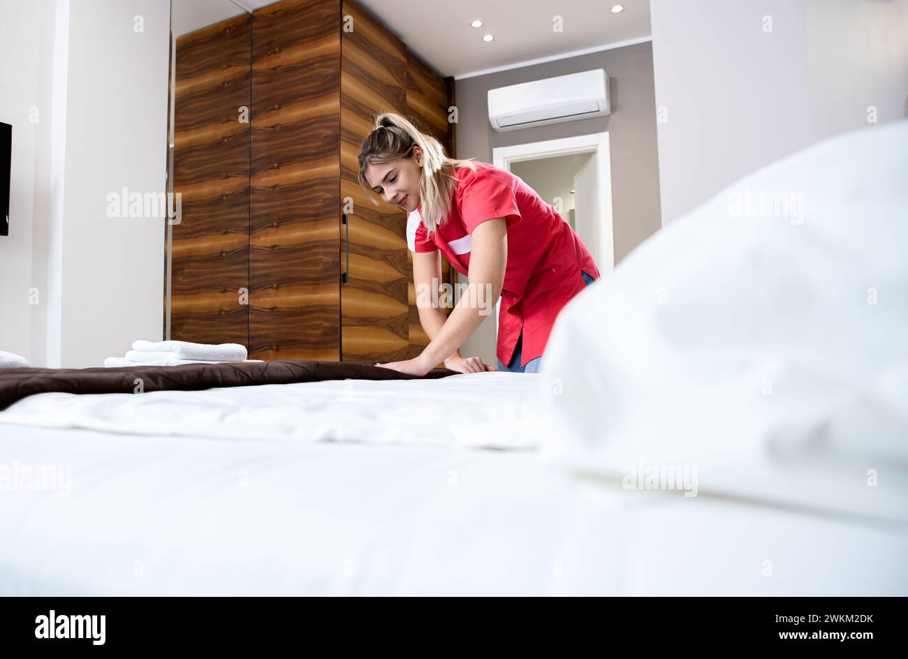 Das lächelnde Zimmermädchen wechselte die Bettwäsche auf dem Bett in einem Hotelzimmer. Stockfoto