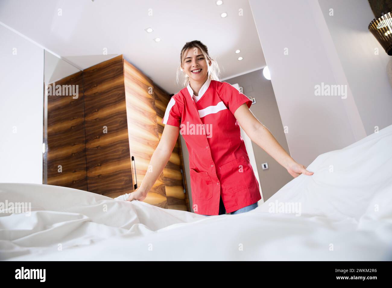 Das lächelnde Zimmermädchen wechselte die Bettwäsche auf dem Bett in einem Hotelzimmer. Stockfoto