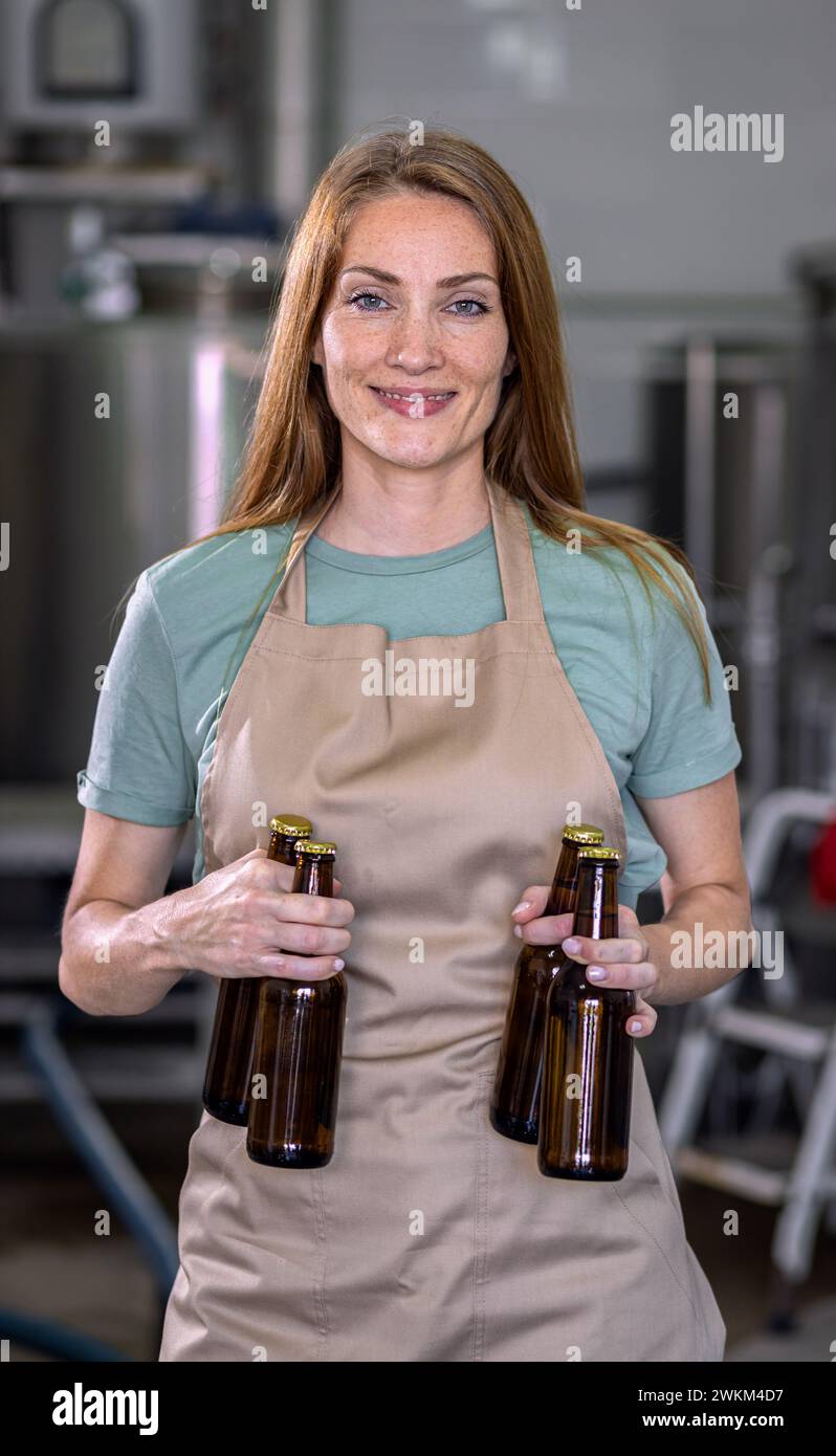 Porträt einer Brauerin in der Handwerksbrauerei, die eine Bierflasche hält. Stockfoto