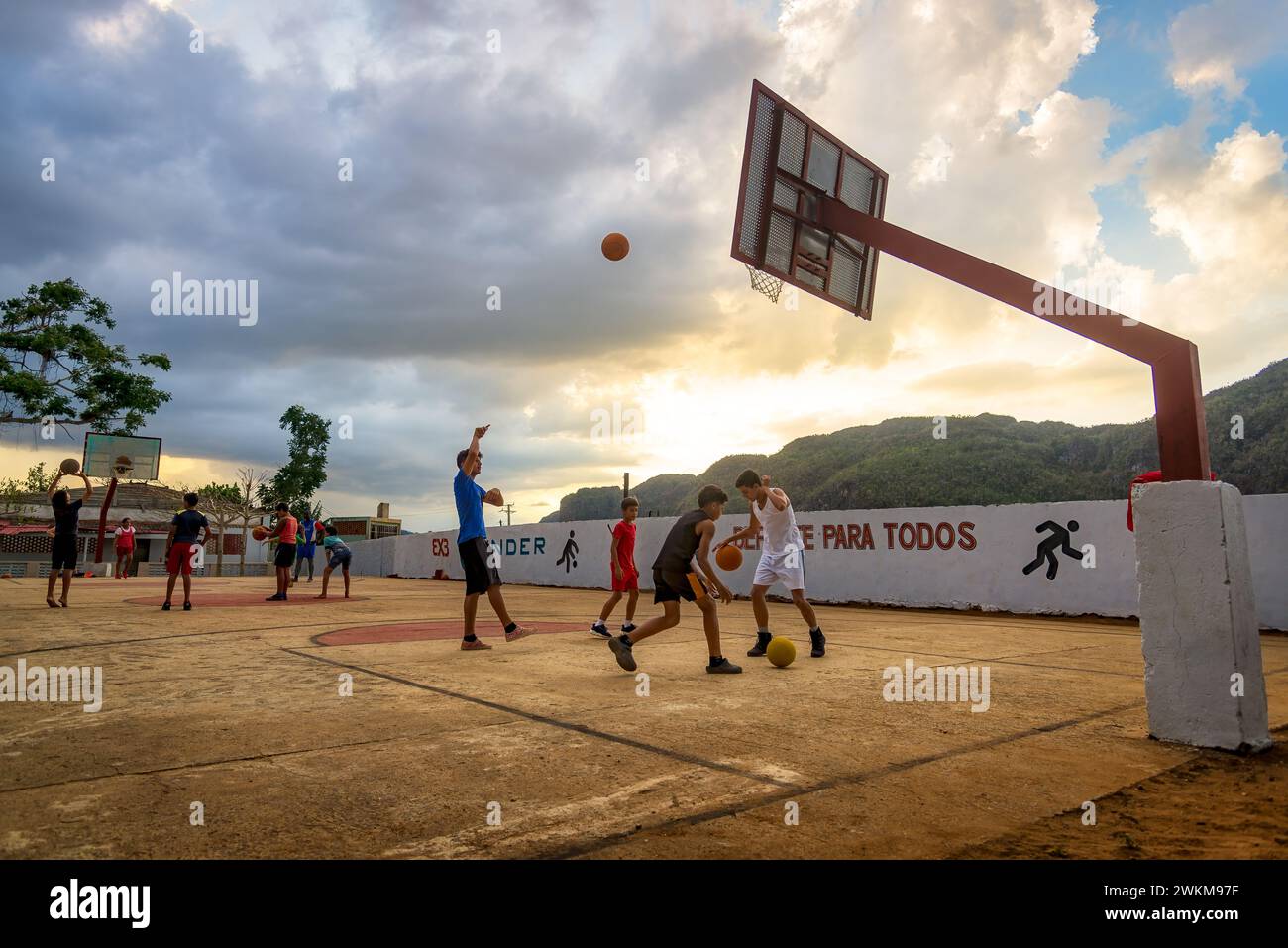 Vinales, Kuba - 6. Februar 2023: Lokale Jungen stellen sich bei Sonnenuntergang in einem dynamischen Outdoor-Basketballspiel vor. Berge im Hintergrund Stockfoto