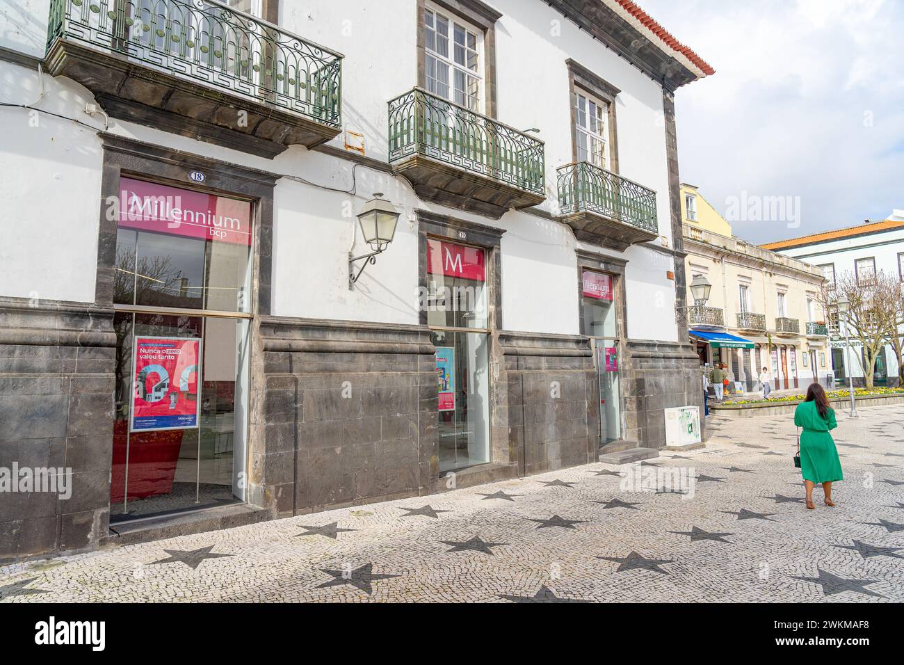 Seitenfassade der Jahrtausendbank, Frau in grünem Kleid geht, Ponta Delgada-Azores-Portugal.3-2024 Stockfoto