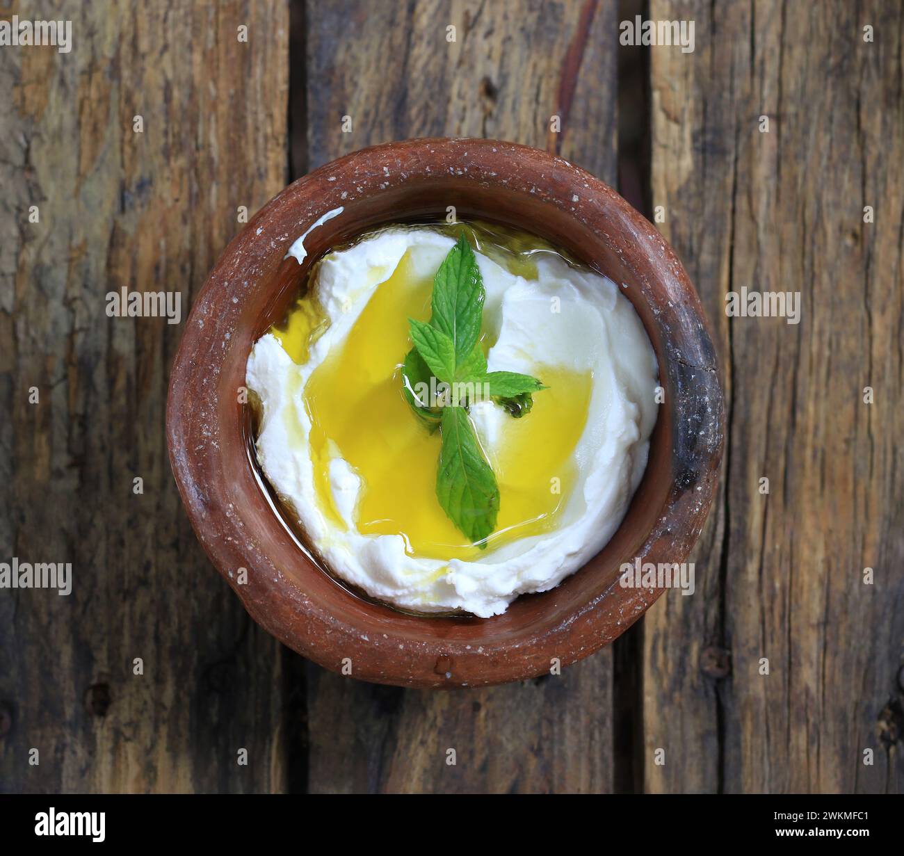 Eine Töpferschale Labneh, garniert mit Olivenöl und Minze auf einem Holztisch. Stockfoto