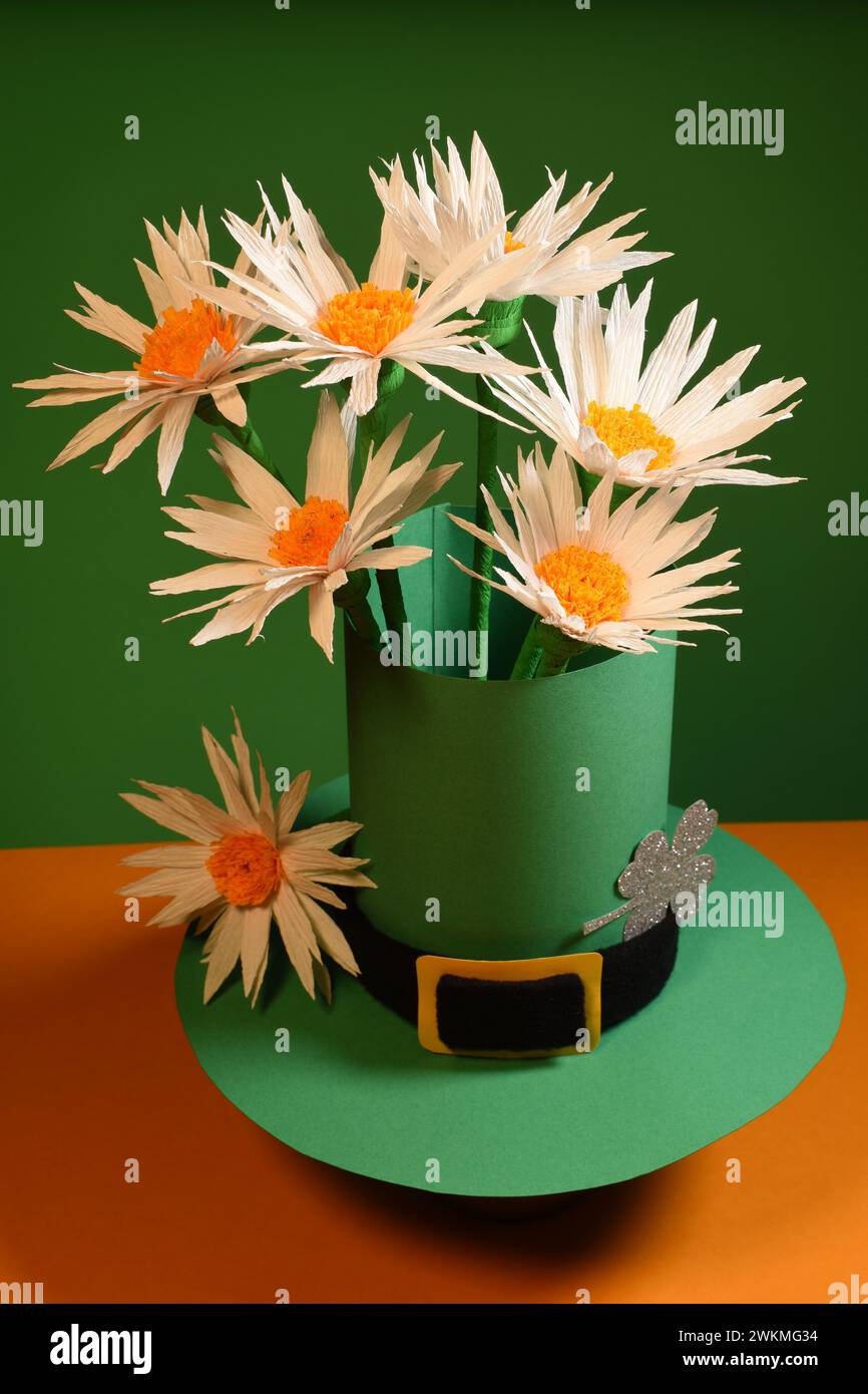 Grüner St. Patrick's Hut mit Gänseblümchen auf grünem und orangefarbenem Hintergrund Stockfoto