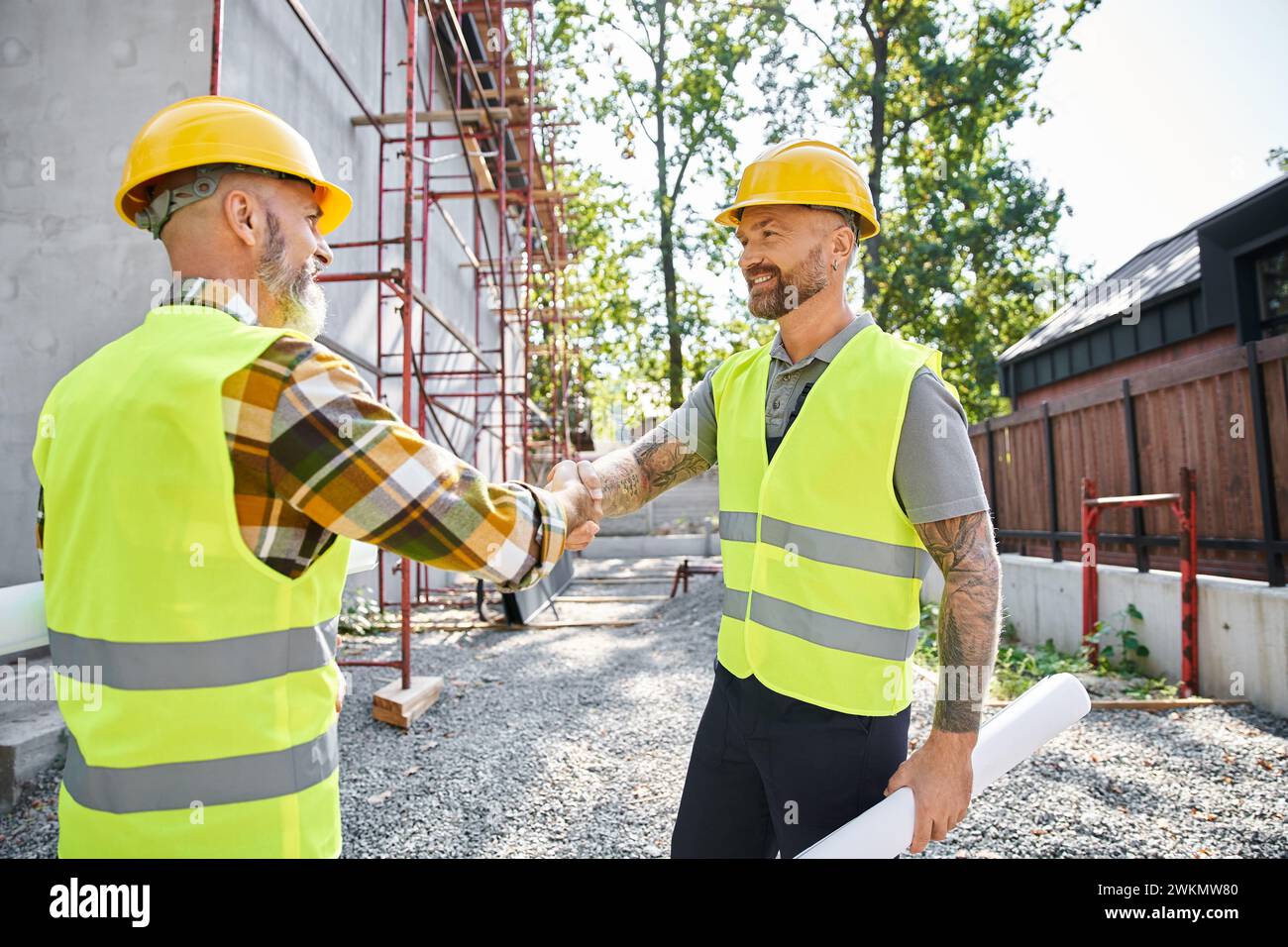 Fröhliche Bauarbeiter schütteln sich die Hände und lächeln einander an, Hüttenbauer Stockfoto