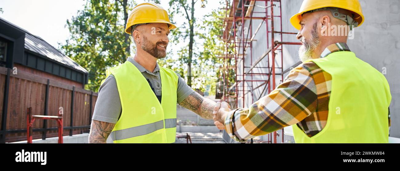 Lustige Bauarbeiter schütteln sich die Hände und lächeln einander an, Hüttenbauer, Banner Stockfoto