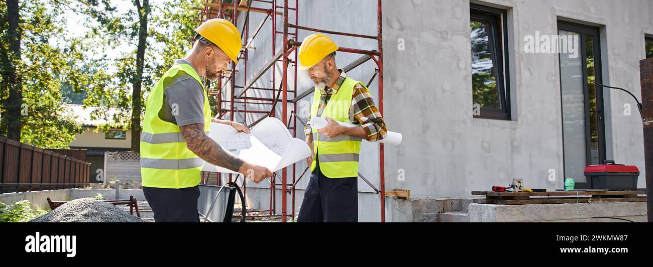 Attraktive Hüttenbauer in Sicherheitswesten, die auf der Baustelle an ihren Bauplänen arbeiten, Banner Stockfoto