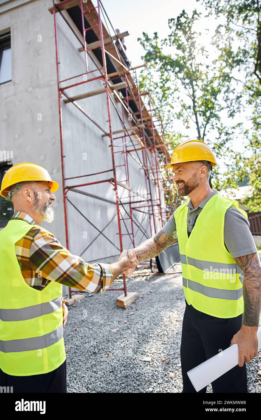 Fröhliche Bauarbeiter schütteln sich die Hände und lächeln einander an, Hüttenbauer Stockfoto