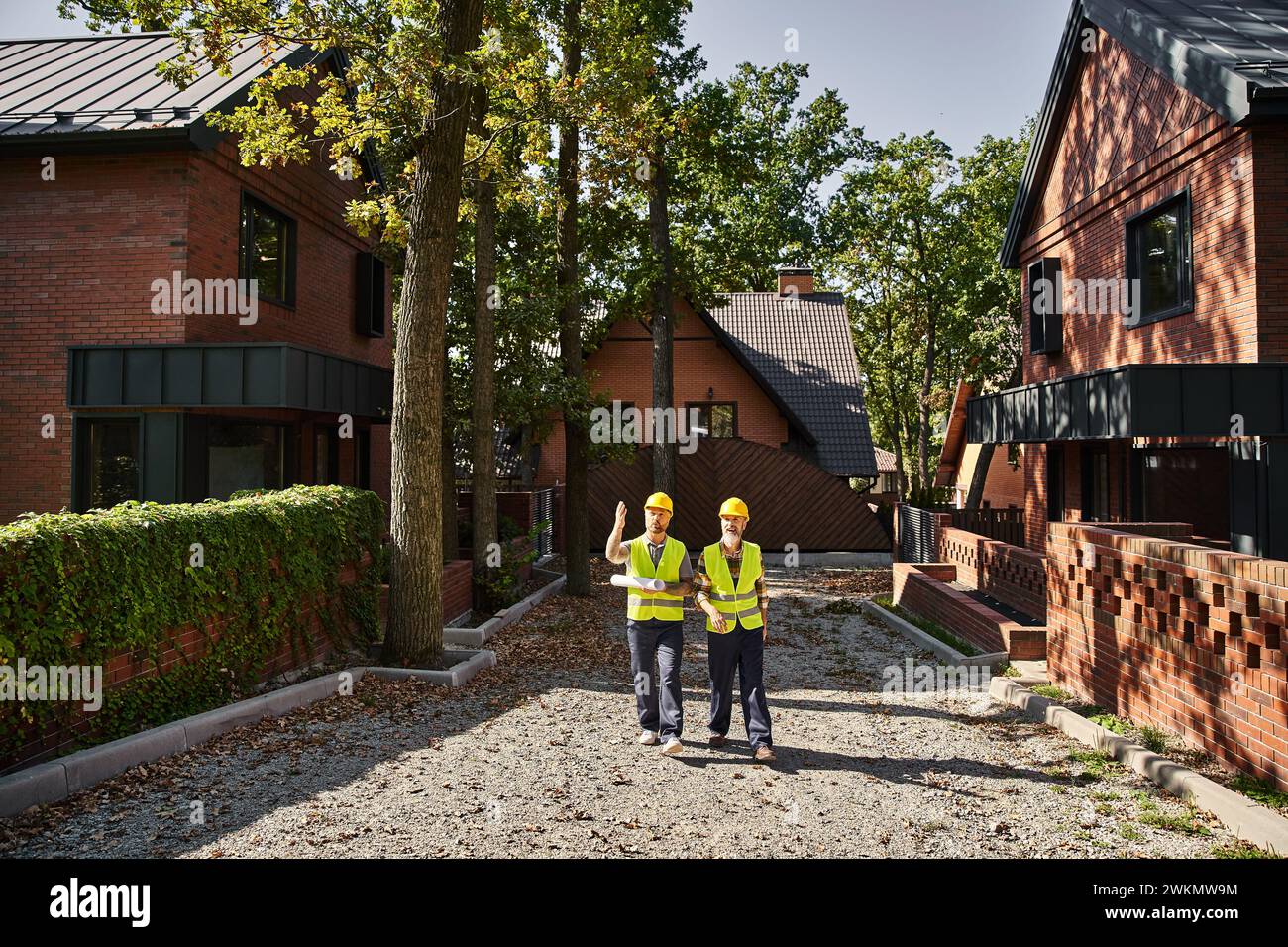 Gut aussehende Bauarbeiter in Schutzhelmen gehen und diskutieren Baustelle, Hüttenbauer Stockfoto