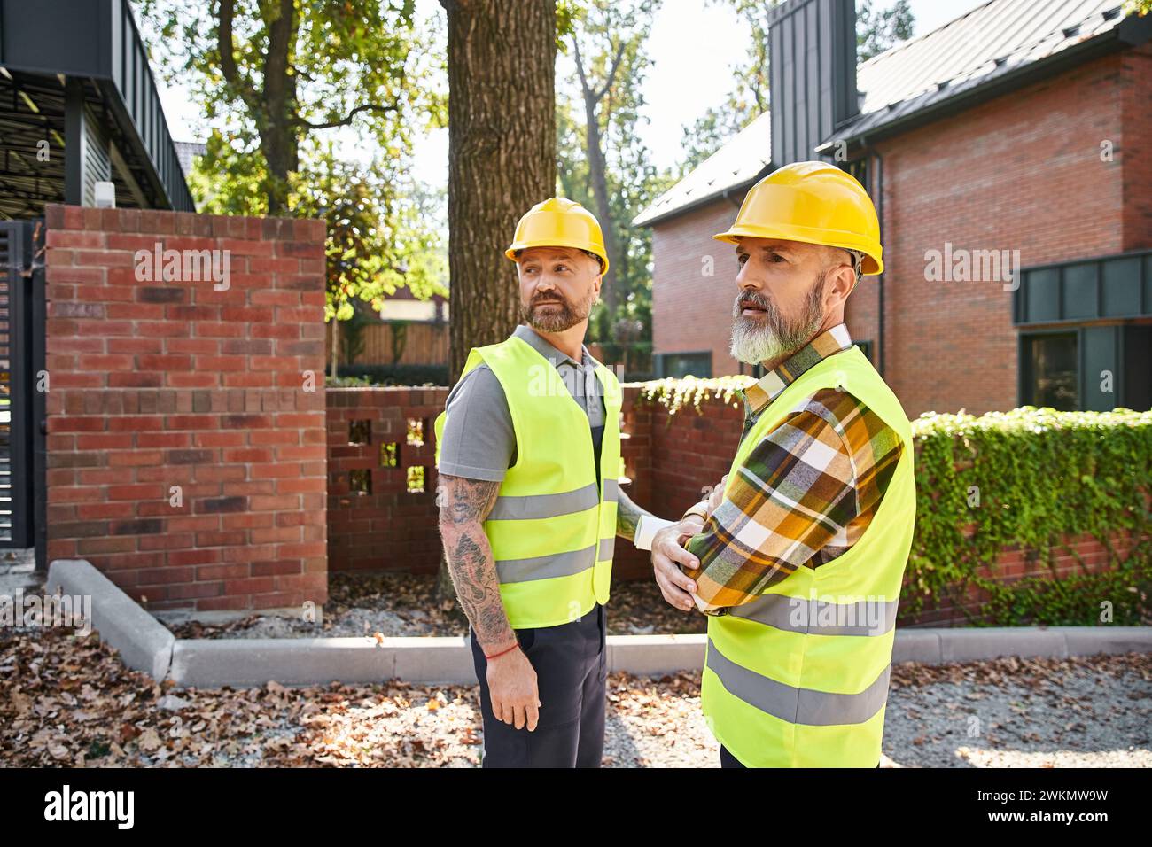 Attraktive Bauarbeiter in Schutzhelmen gehen und diskutieren Baustelle, Hüttenbauer Stockfoto