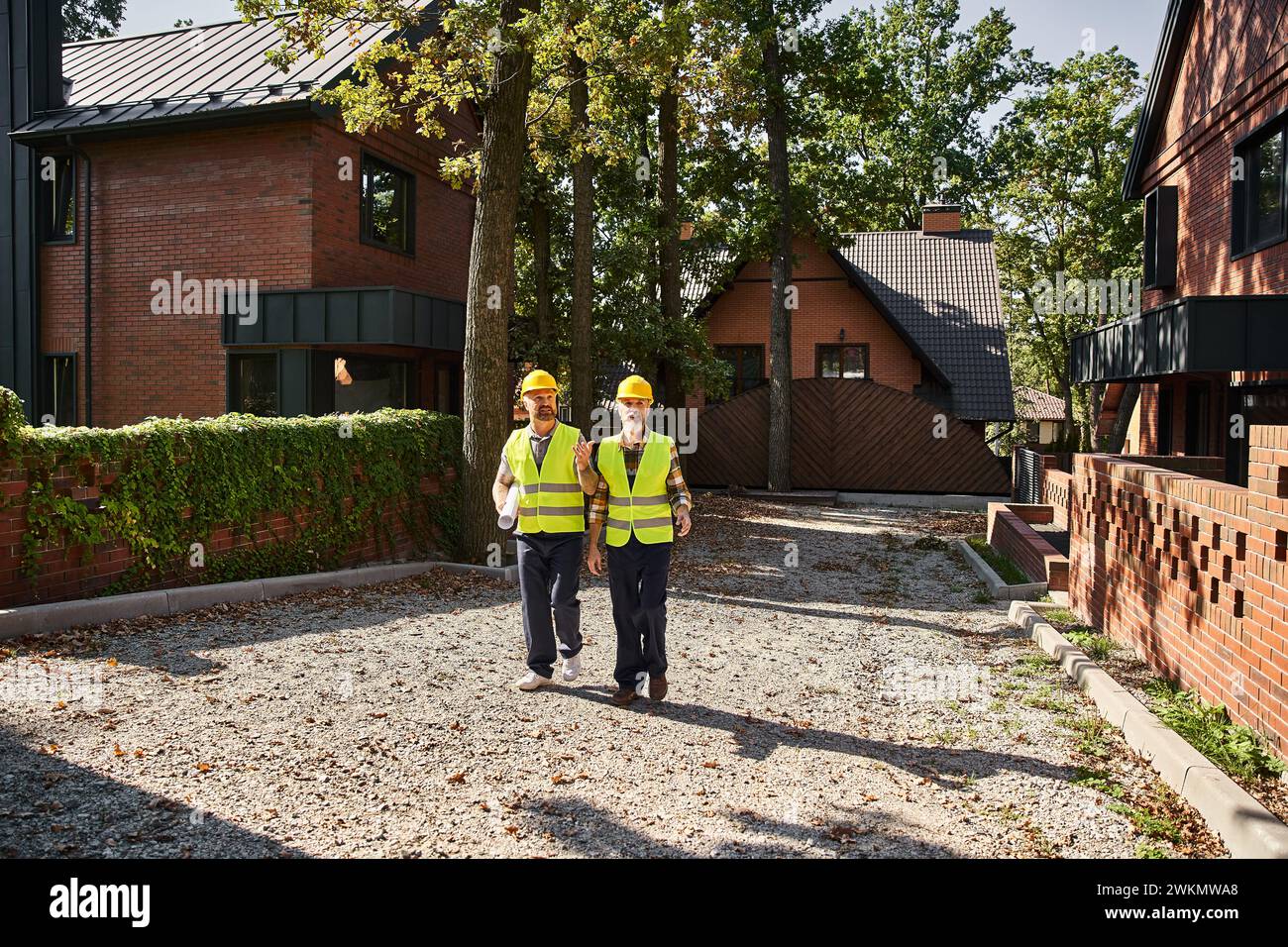 Gut aussehende Bauarbeiter in Schutzhelmen gehen und diskutieren Baustelle, Hüttenbauer Stockfoto
