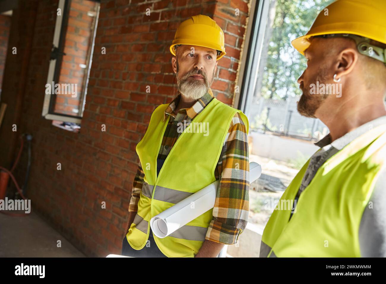Gutaussehende Bauarbeiter in Schutzhelmen arbeiten vor Ort zusammen, Hüttenbauer Stockfoto
