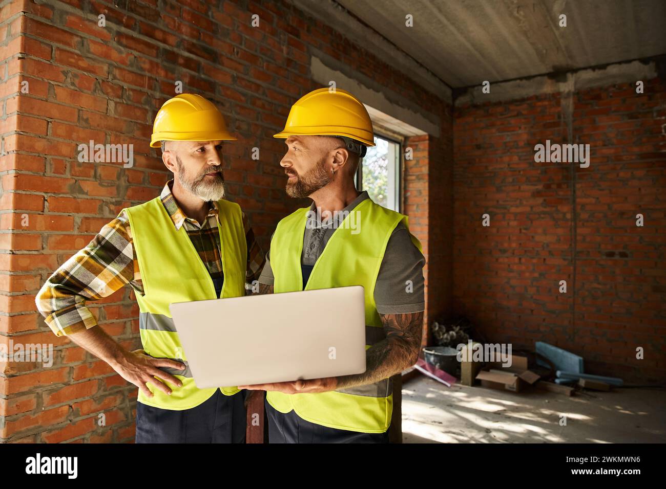 Fleißige Bauarbeiter in Sicherheitswesten, die vor Ort mit Laptop arbeiten, Hüttenbauer Stockfoto