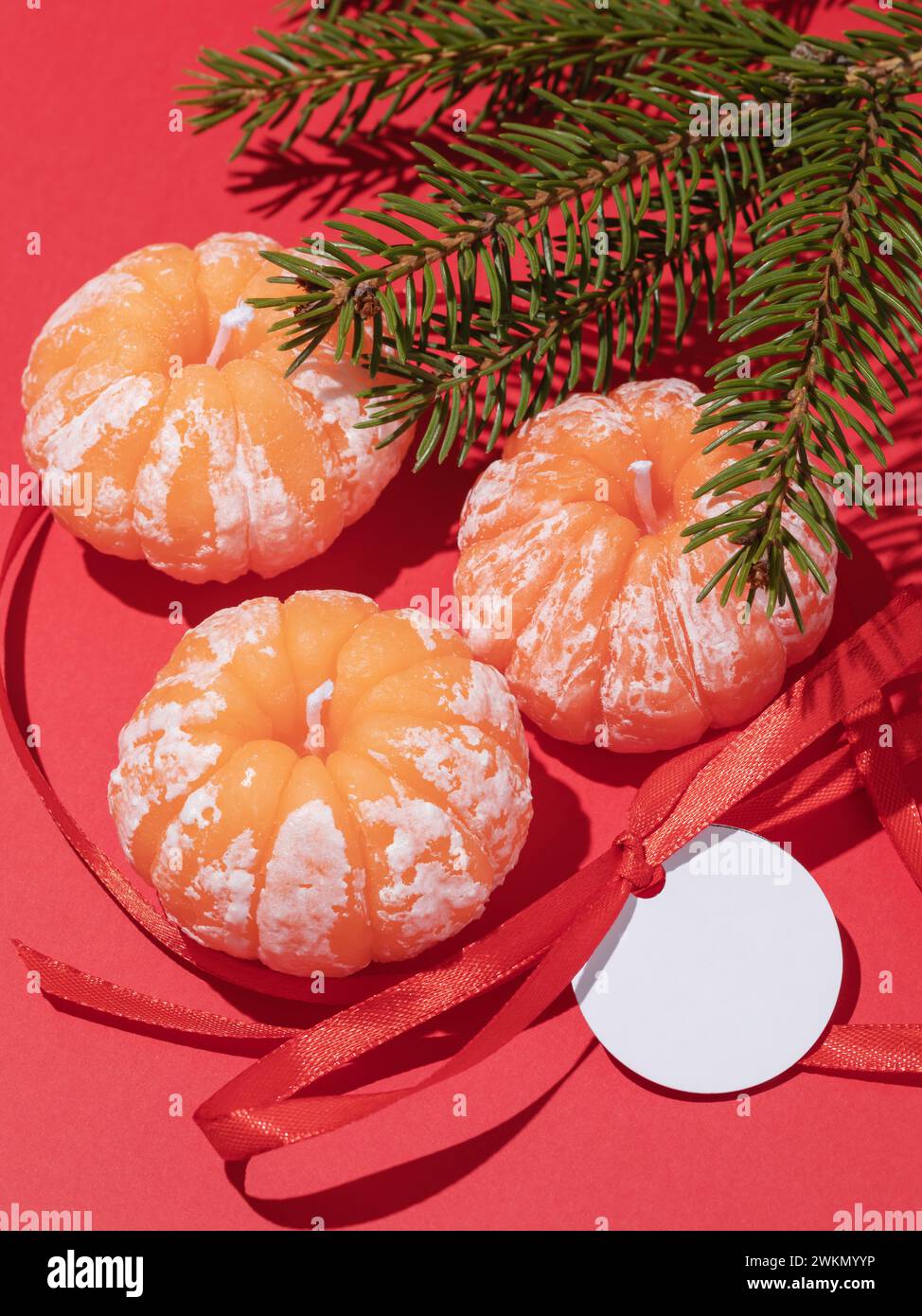 Dekorative aromatische Kerzen in Form von Mandarinen und Tannenzweig auf rotem Hintergrund Stockfoto