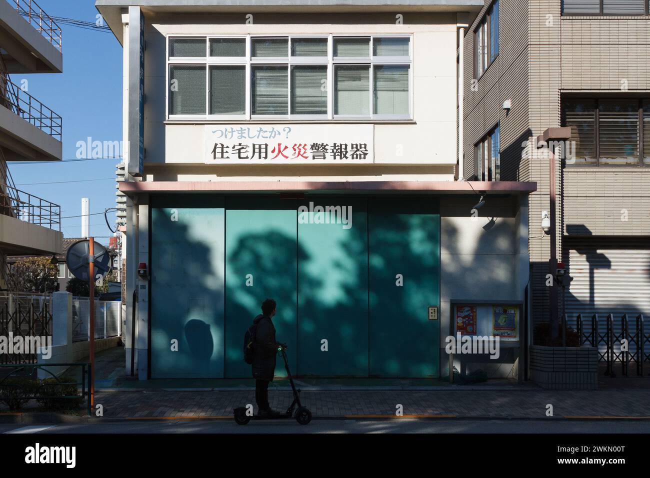 Ein Tourist fährt ein E-Roller klebte die Tür der Feuerwehr in einer Seitenstraße von Mejiro, Tokio, Japan. Stockfoto