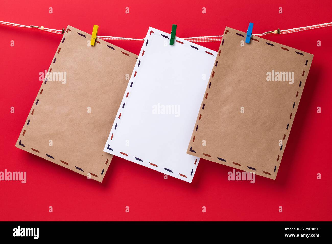 Drei Glückwunschumschläge, die mit Kleiderschränken befestigt sind und an einem Seil auf rotem Hintergrund hängen, Vorlage für Designer Stockfoto