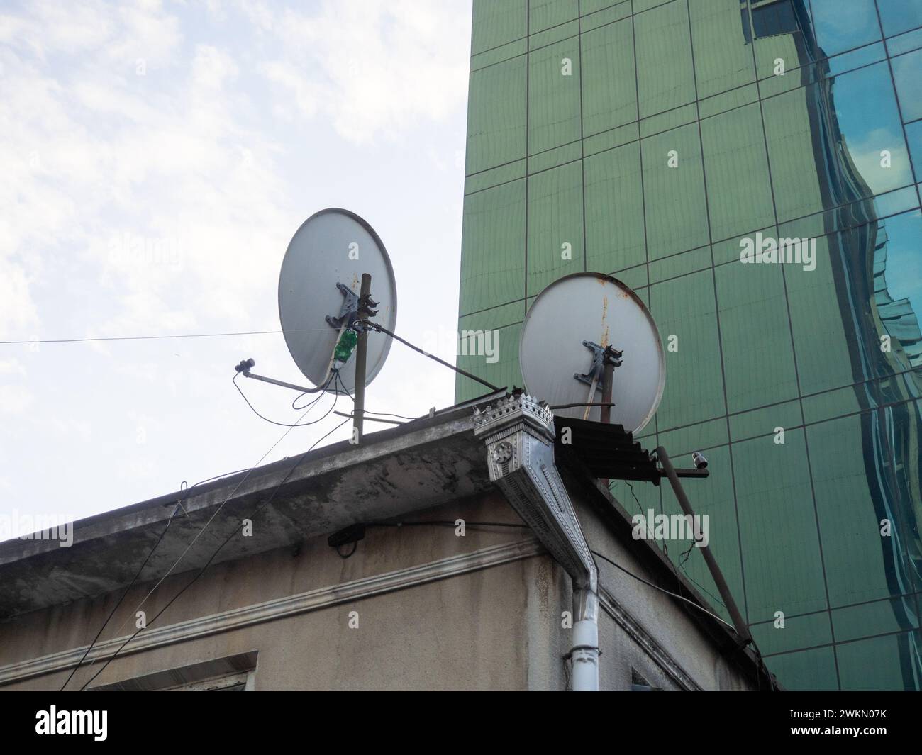 Satellitenschüsseln auf einem alten Dach. Empfang eines Fernsehsignals. Asien. Drähte an einem Stab. Strom auf der Straße. Konzept Stockfoto