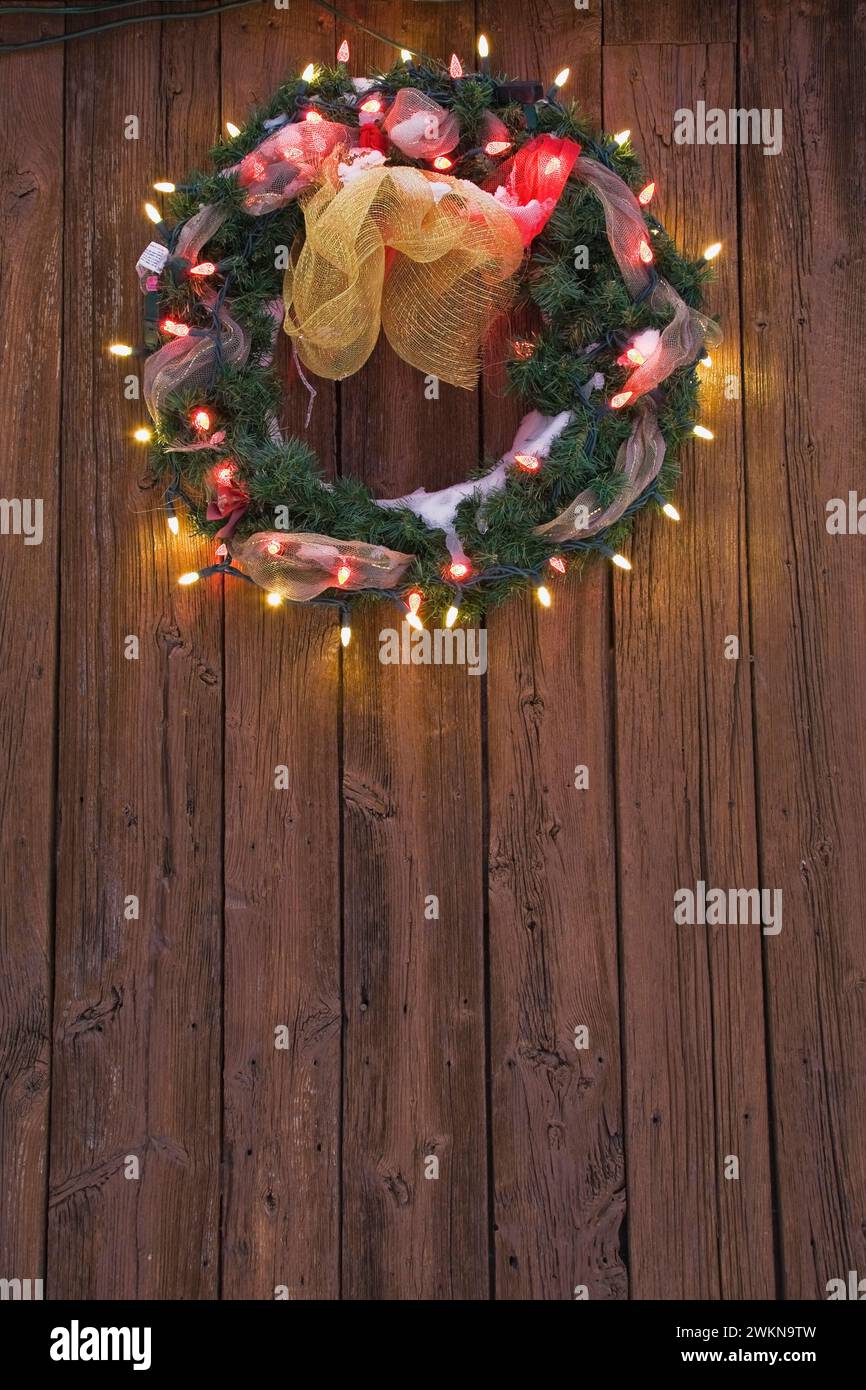 Nahaufnahme des beleuchteten Weihnachtskranzes auf Holzdielen des Lagerhauses in der Dämmerung im Winter. Stockfoto