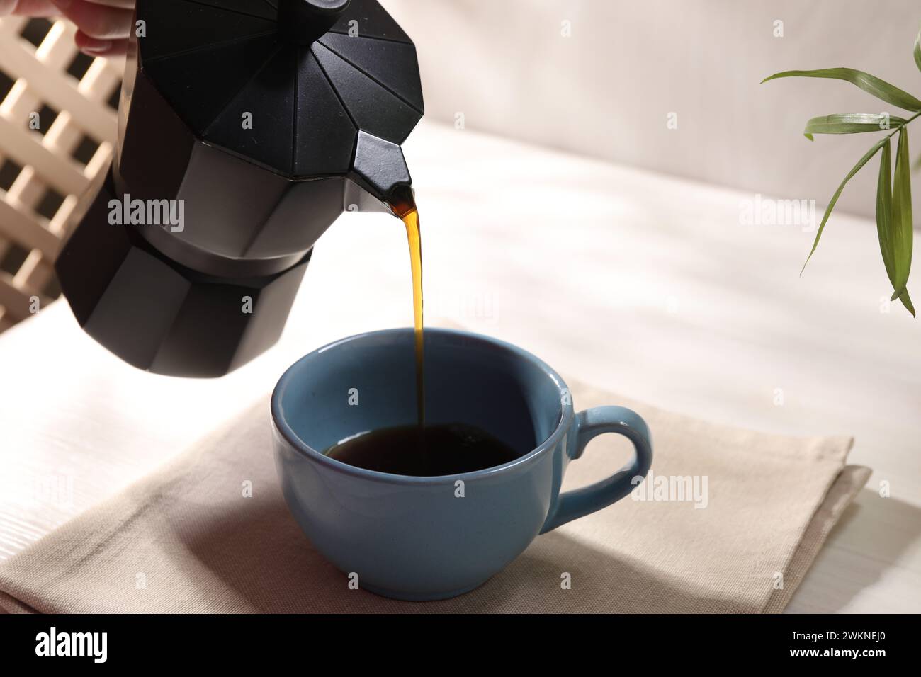 Aromatischen Kaffee aus der Mokakanne in eine Tasse am weißen Tisch gießen, Nahaufnahme Stockfoto