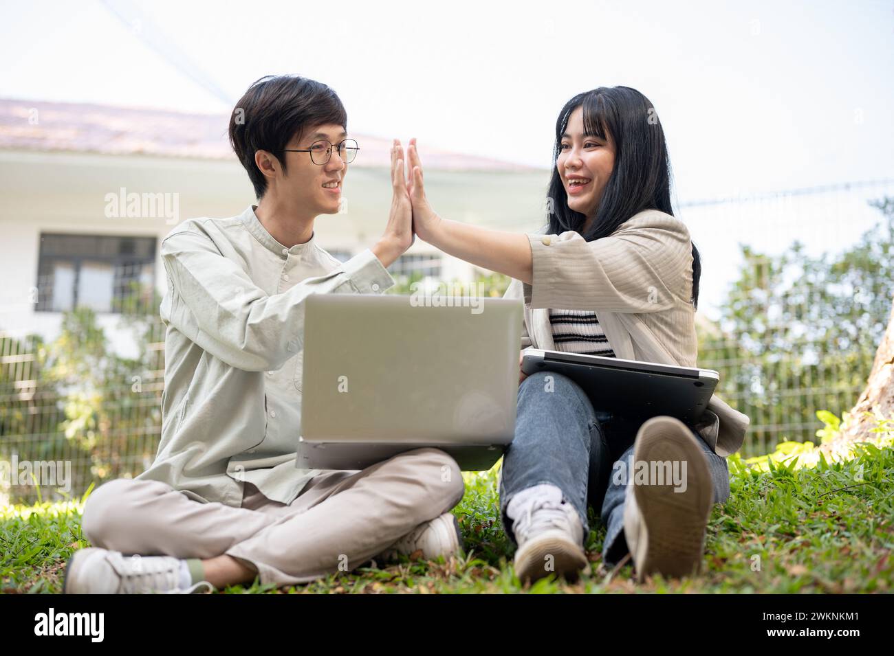 Zwei fröhliche asiatische Universitätsstudenten geben sich gegenseitig fünf, feiern ihren Projekterfolg oder testen gemeinsam auf t Stockfoto