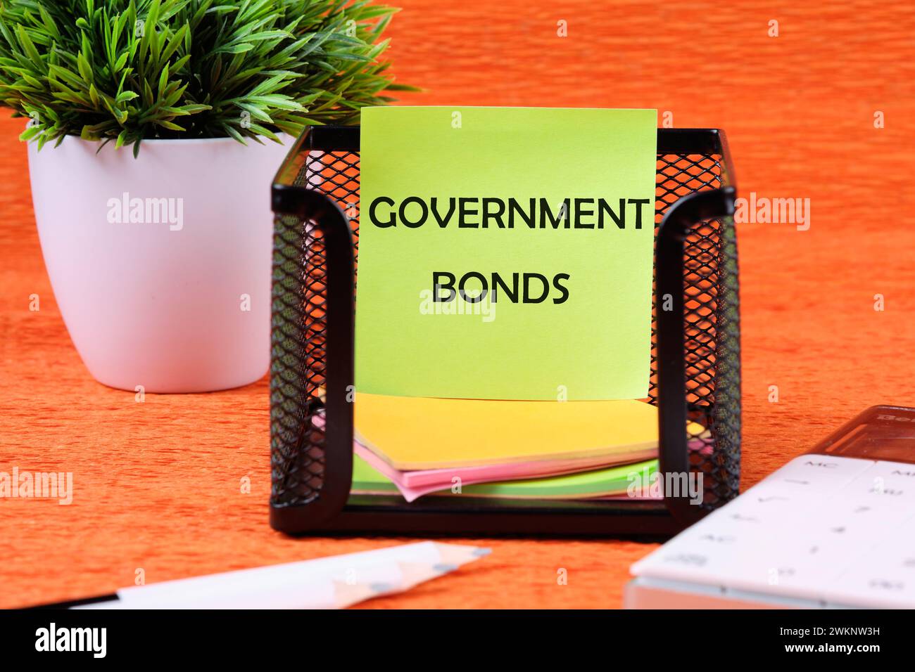 Text für Staatsanleihen auf einem grünen Aufkleber neben Bürobedarf auf orangem Hintergrund Stockfoto