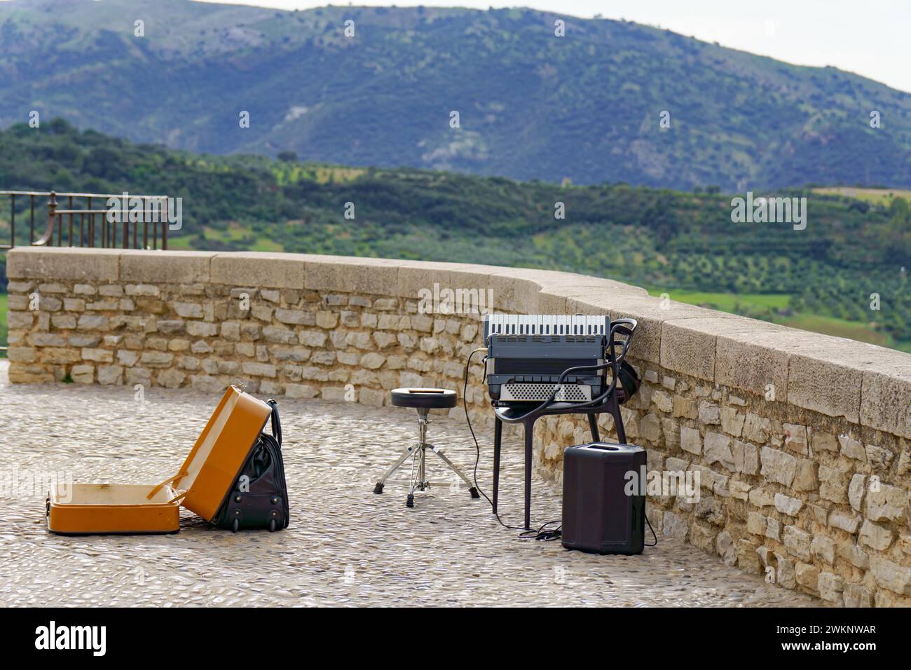 Ein Straßenmusiker spielt Akkordeon mit einer bergigen Landschaft im Hintergrund Stockfoto