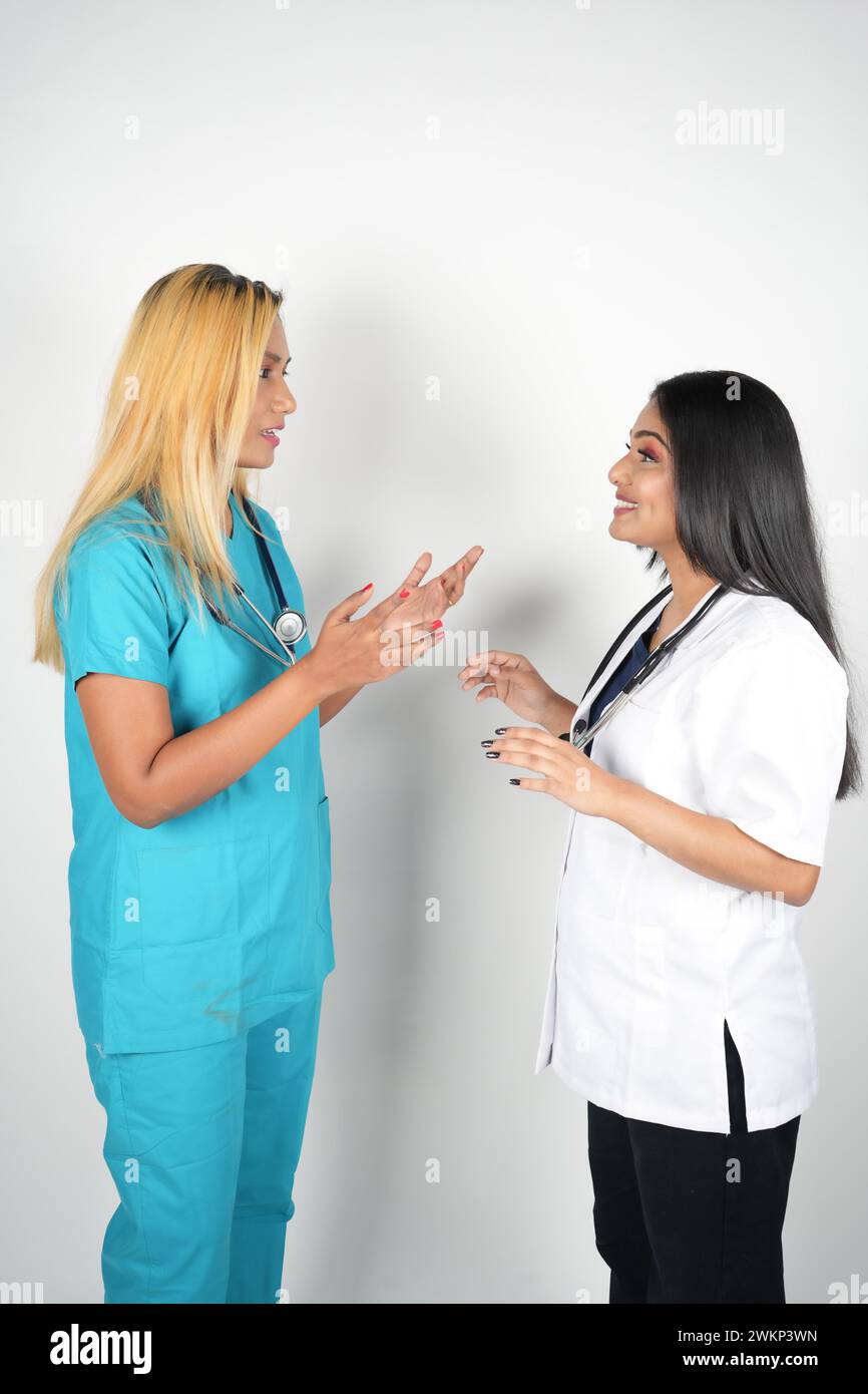 Zwei Ärztinnen, die sich unterhalten, tragen Peelings und weiße Oberteile vor einem neutralen grauen Hintergrund Stockfoto