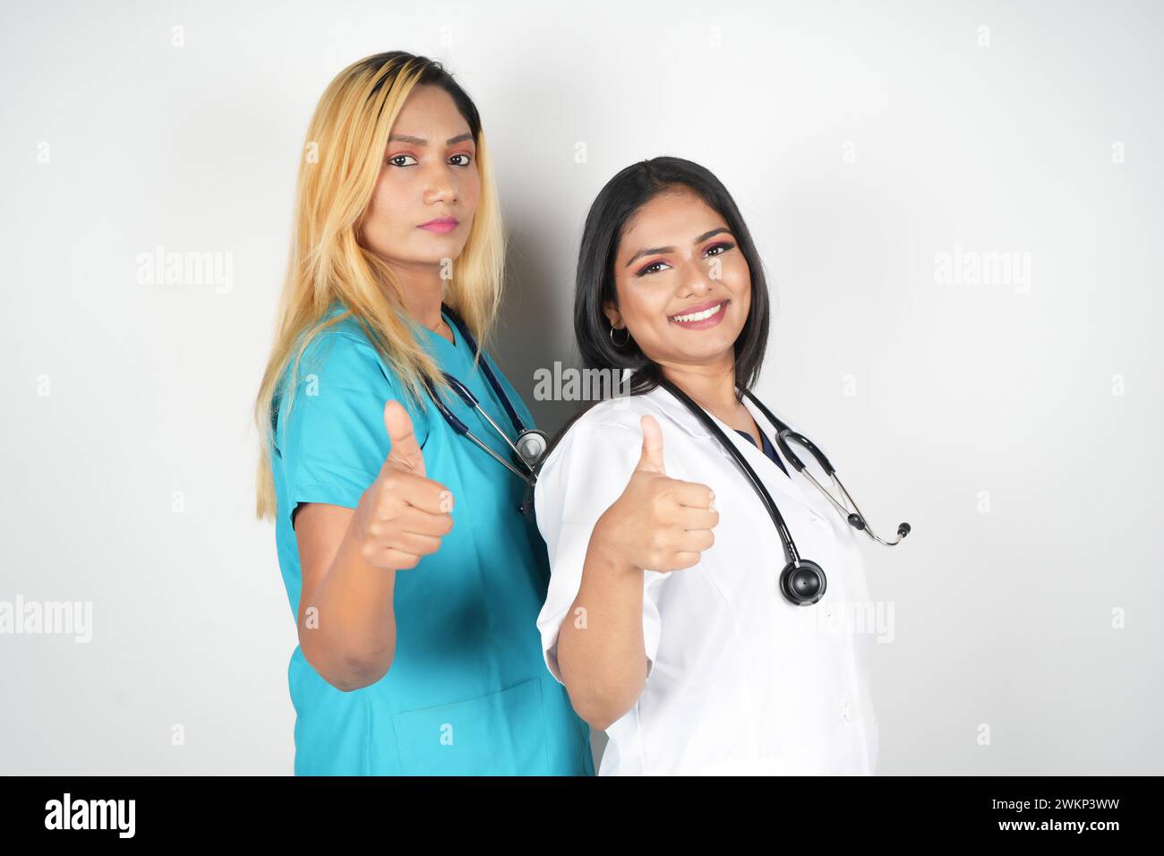 Zwei weibliche Gesundheitsfachkräfte in Scheueranzügen halten den Daumen nach oben zur Kamera Stockfoto