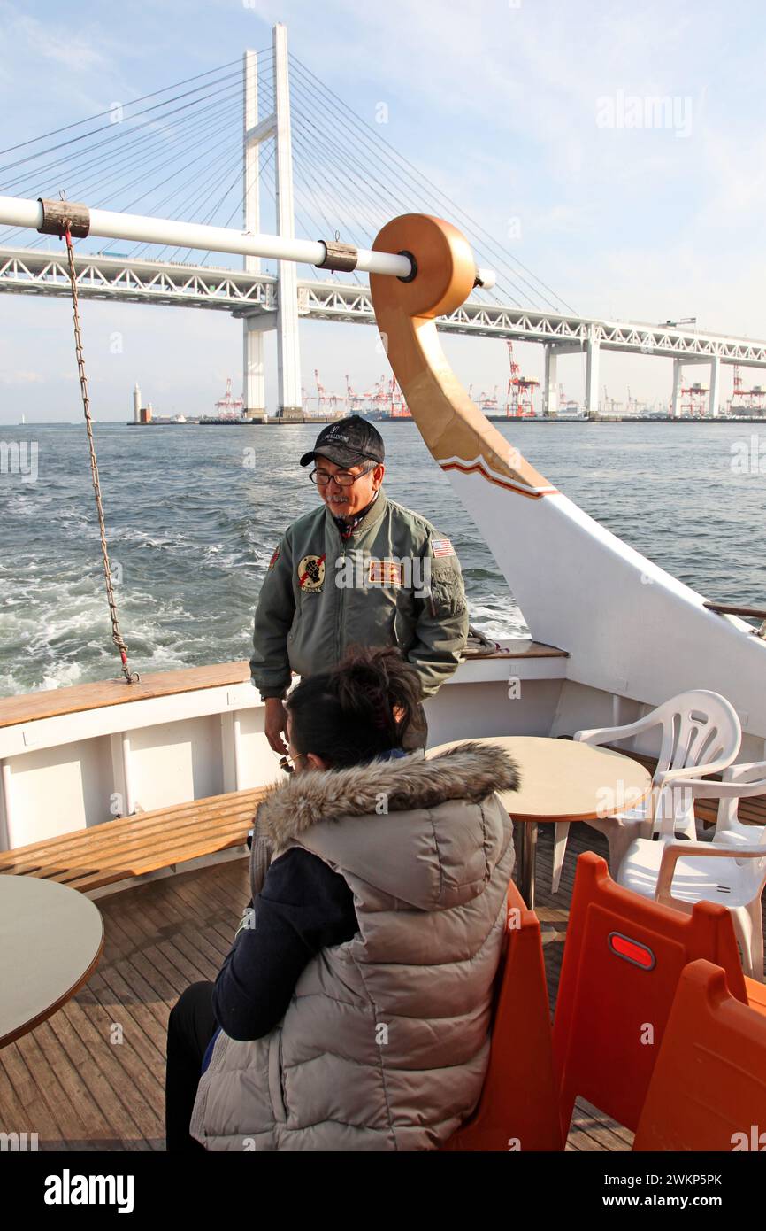 Ein Kreuzfahrtschiff in der Yokohama Bay mit Yokohama Gate Bridge im Hintergrund und einem Passagier im Boot. Stockfoto
