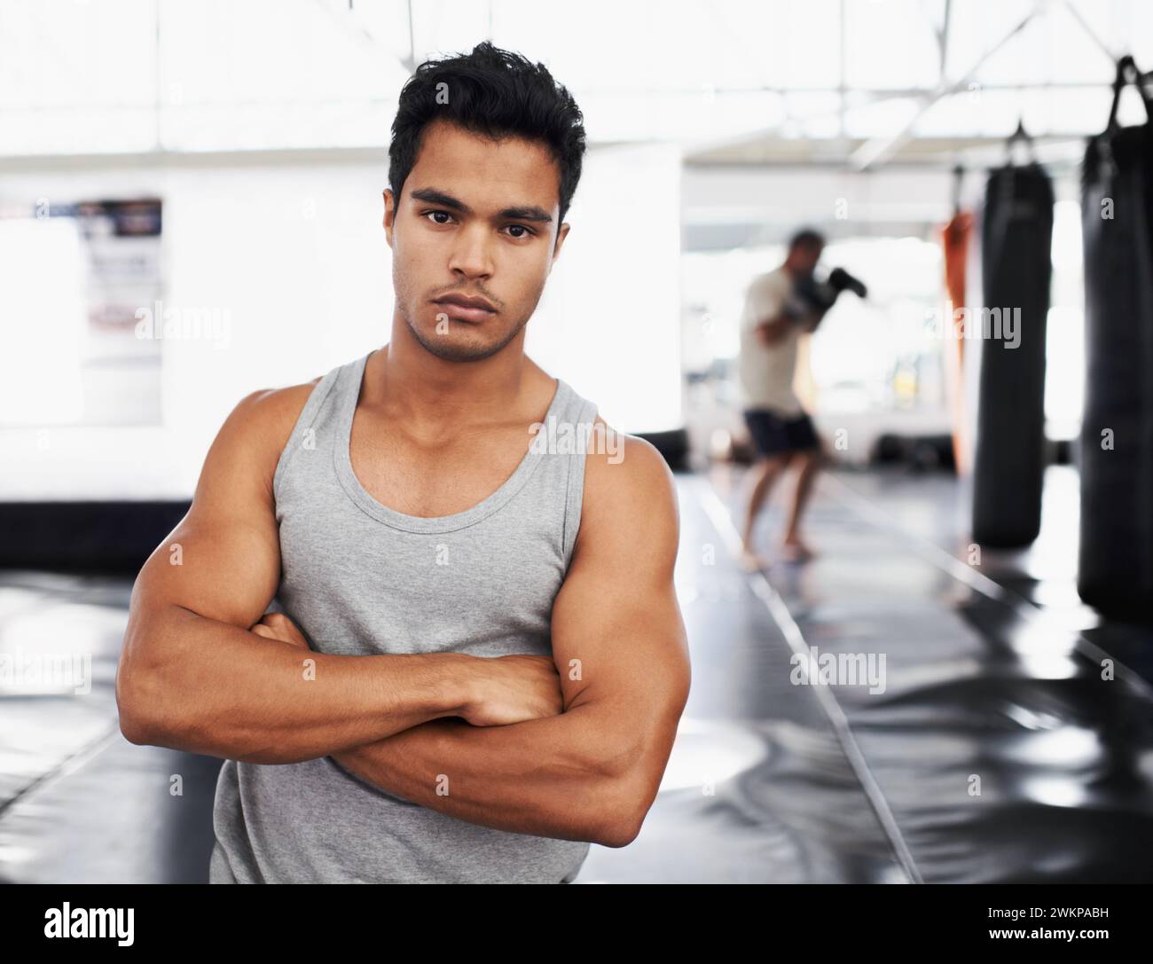 Bewegung, Training und Porträt des Mannes in der Turnhalle für Sport, Praxis oder Wellness für die Gesundheit. Personal Trainer, Gesicht und ernster Ausdruck mit Armen Stockfoto
