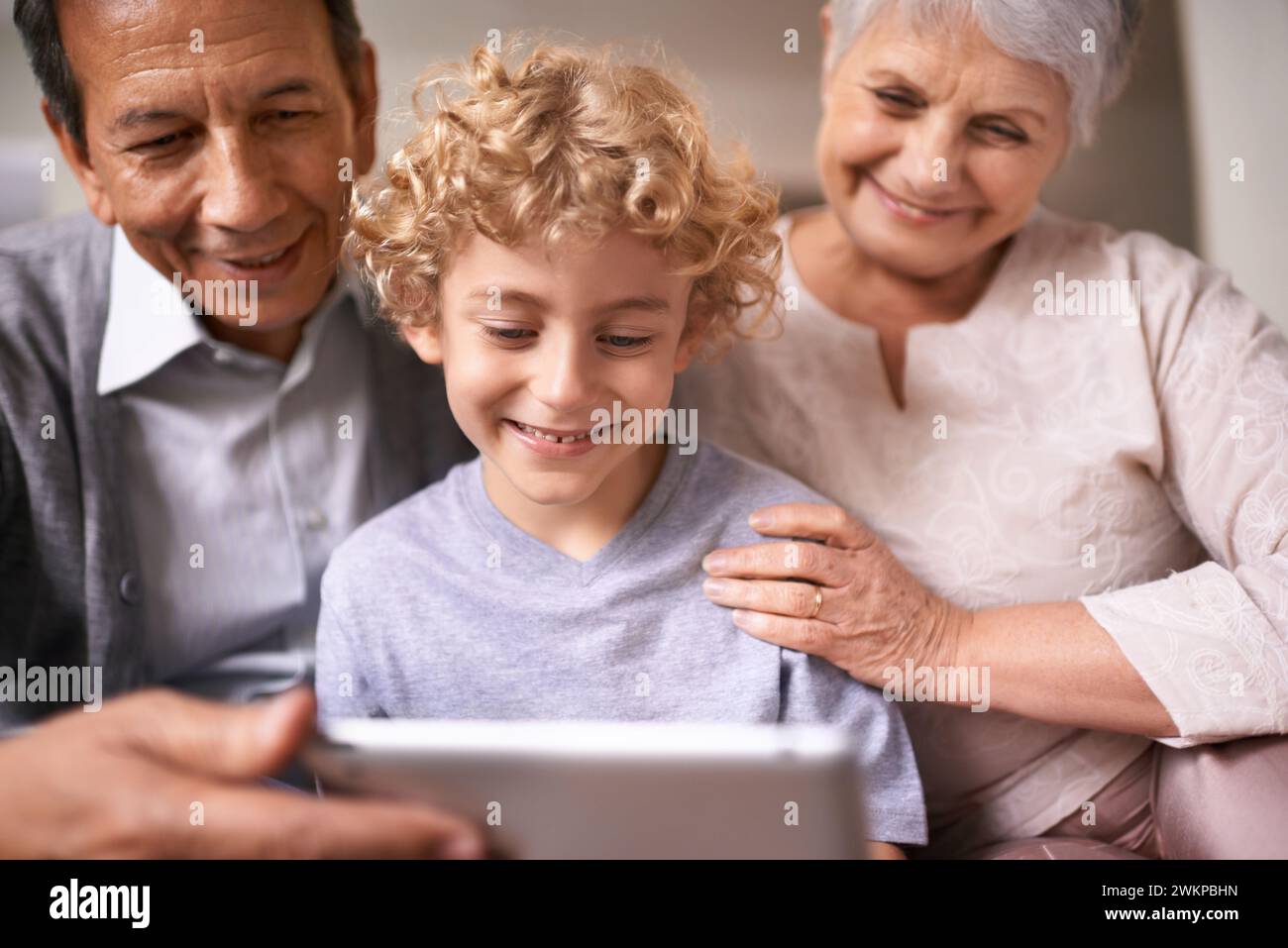 Glückliche Familie, Großeltern und Kind mit Tablet für Unterhaltung, soziale Medien oder Forschung auf dem Sofa zu Hause. Grandma, Opa und kleiner Junge lächeln weiter Stockfoto