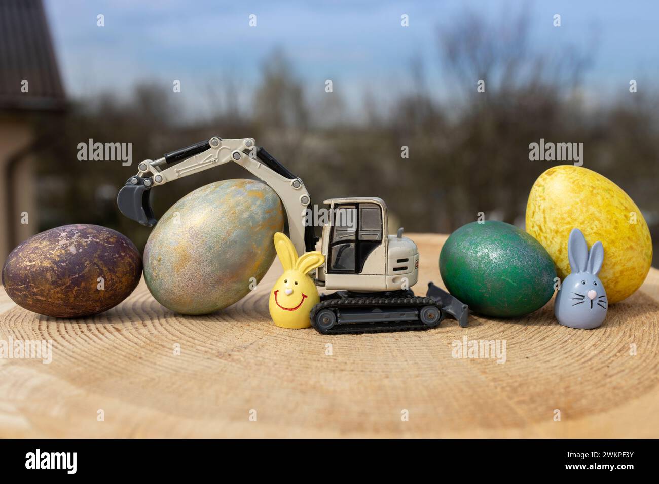 Modell eines spielzeuggrauen Baggers und mehrfarbige Ostereier auf einem Holzstumpf Stockfoto