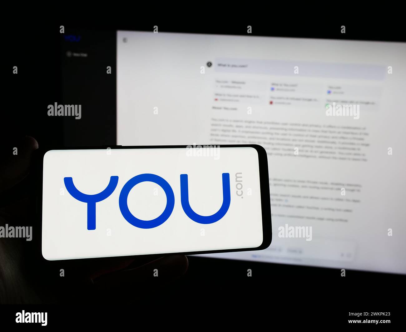 Person, die ein Smartphone mit dem Logo der personalisierten Suchmaschine You.com vor der Website hält. Schwerpunkt auf dem Display des Telefons. Stockfoto