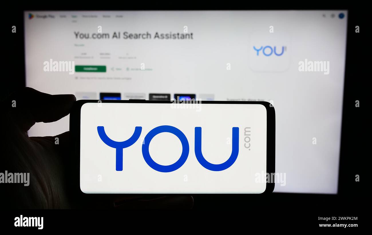 Person, die ein Mobiltelefon mit dem Logo der personalisierten Suchmaschine You.com vor der Webseite des Unternehmens hält. Schwerpunkt auf dem Display des Telefons. Stockfoto